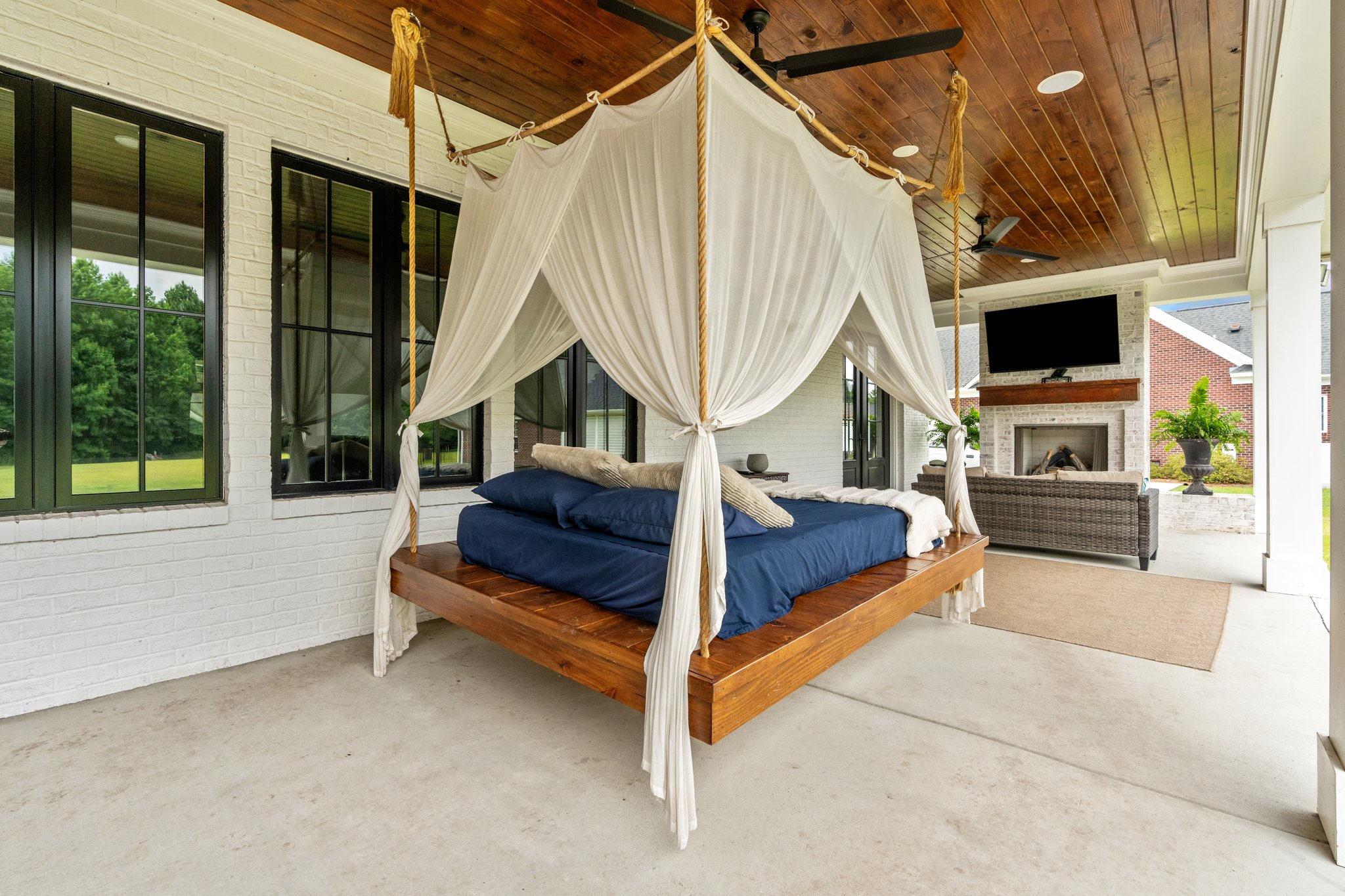 Hanging wooden bed with white curtains on outdoor porch with fireplace