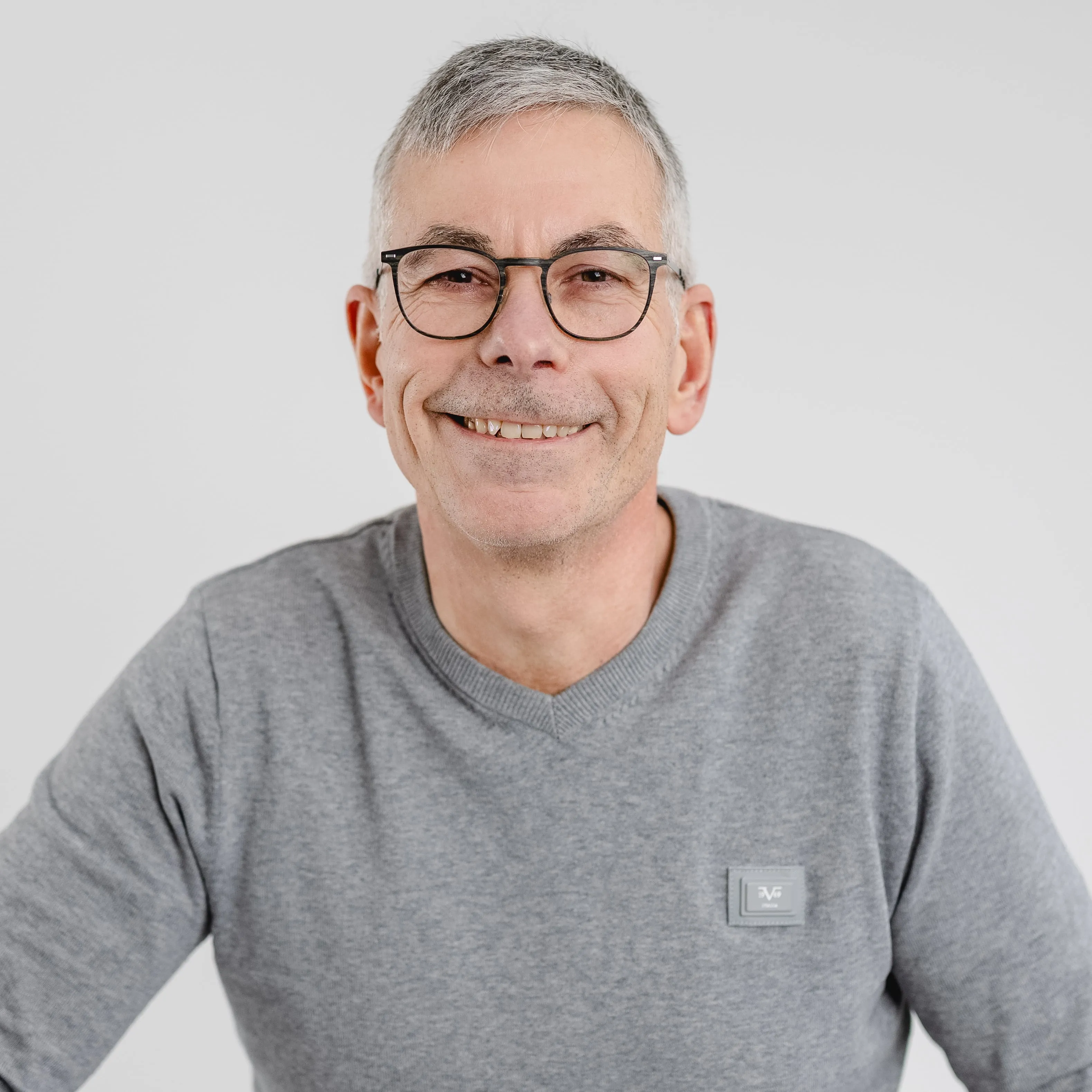 Smiling middle-aged man with short gray hair and glasses wearing a gray sweater.