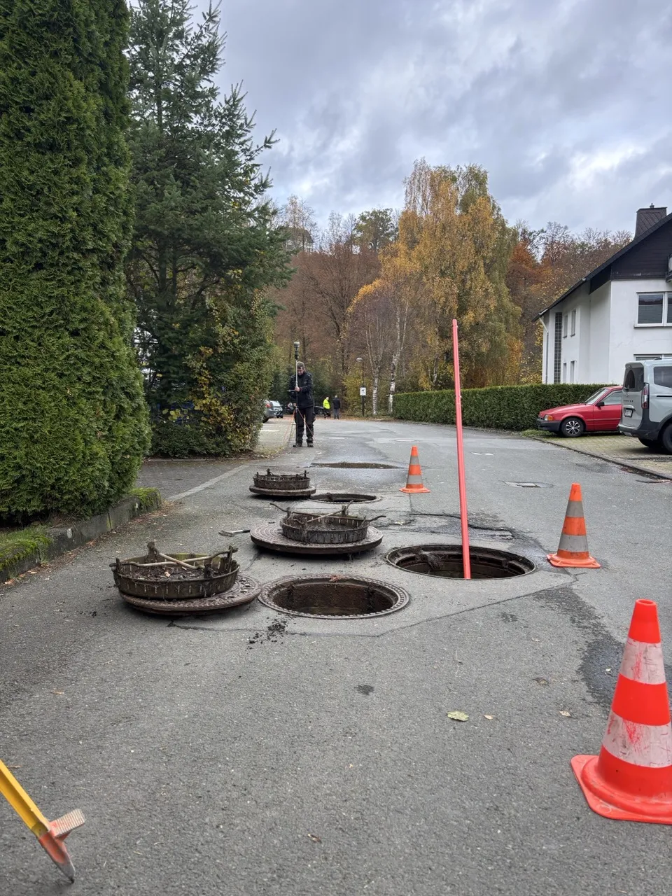 Hands working on a construction report over architectural blueprints with a laptop, glasses, and a white safety helmet on wooden logs.
