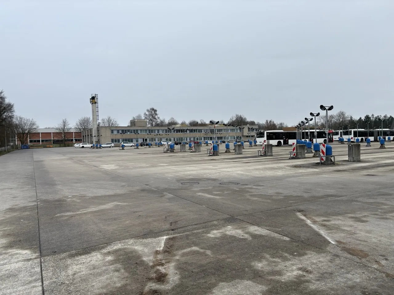 Person reviewing construction blueprints with a laptop, safety helmet, glasses, and clipboard on a wooden surface outdoors.