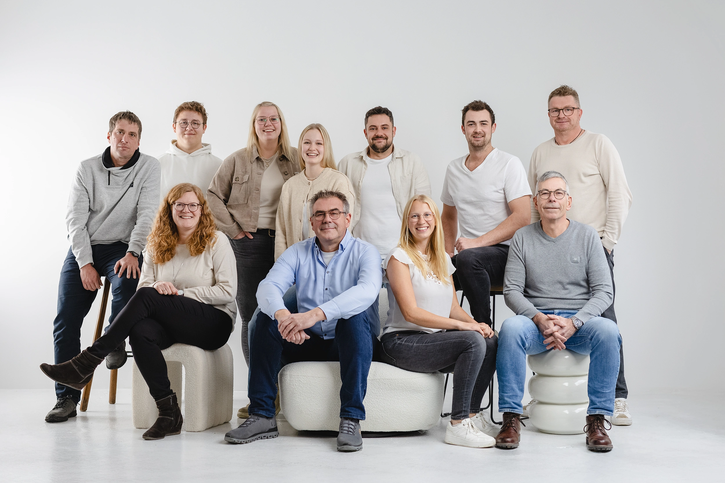 Group of eleven adults, six standing and five seated, posing against a plain white background.