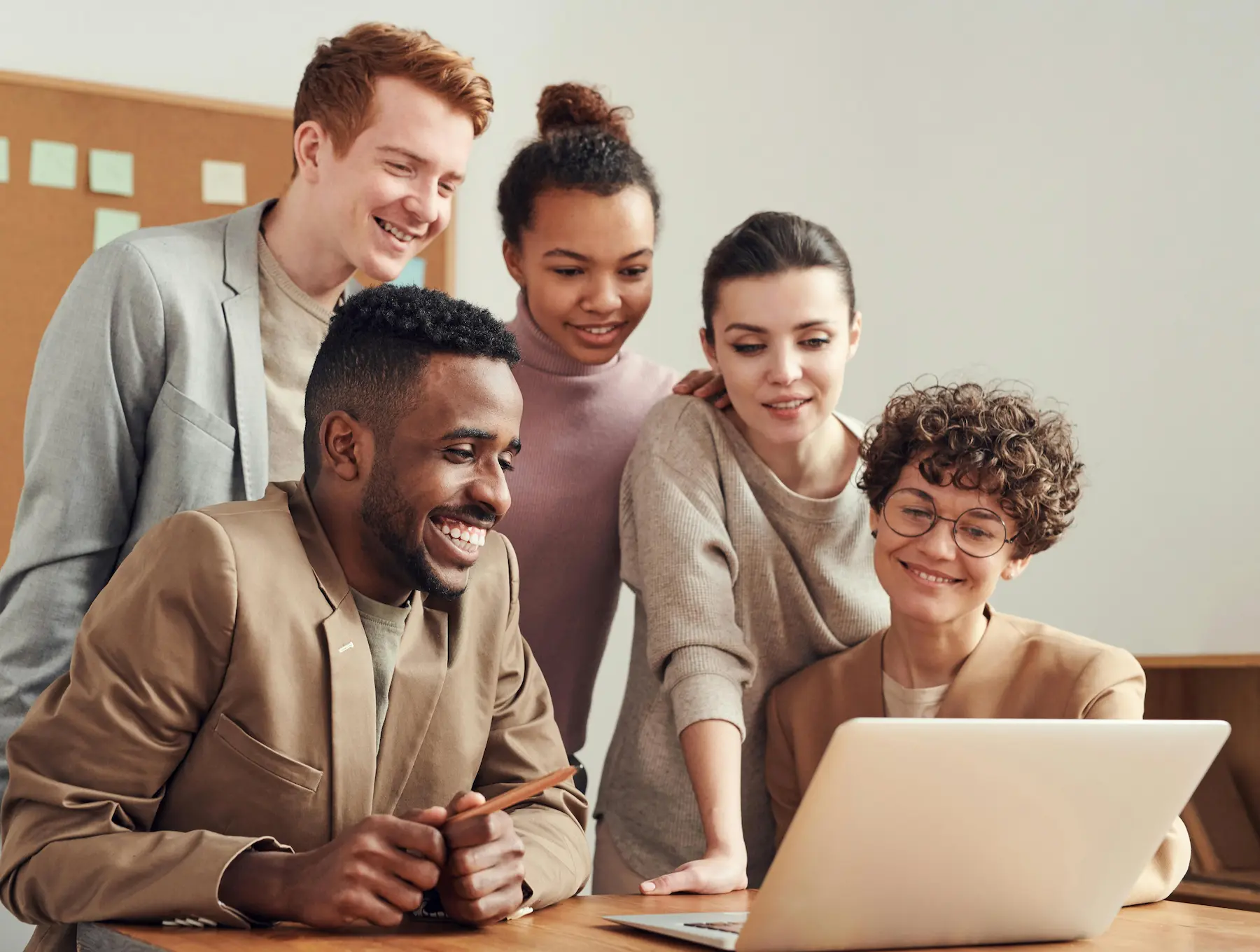 Groupe de collègues souriants réunis autour d’un ordinateur portable lors d’un séminaire à l’hôtel Armes de Champagne