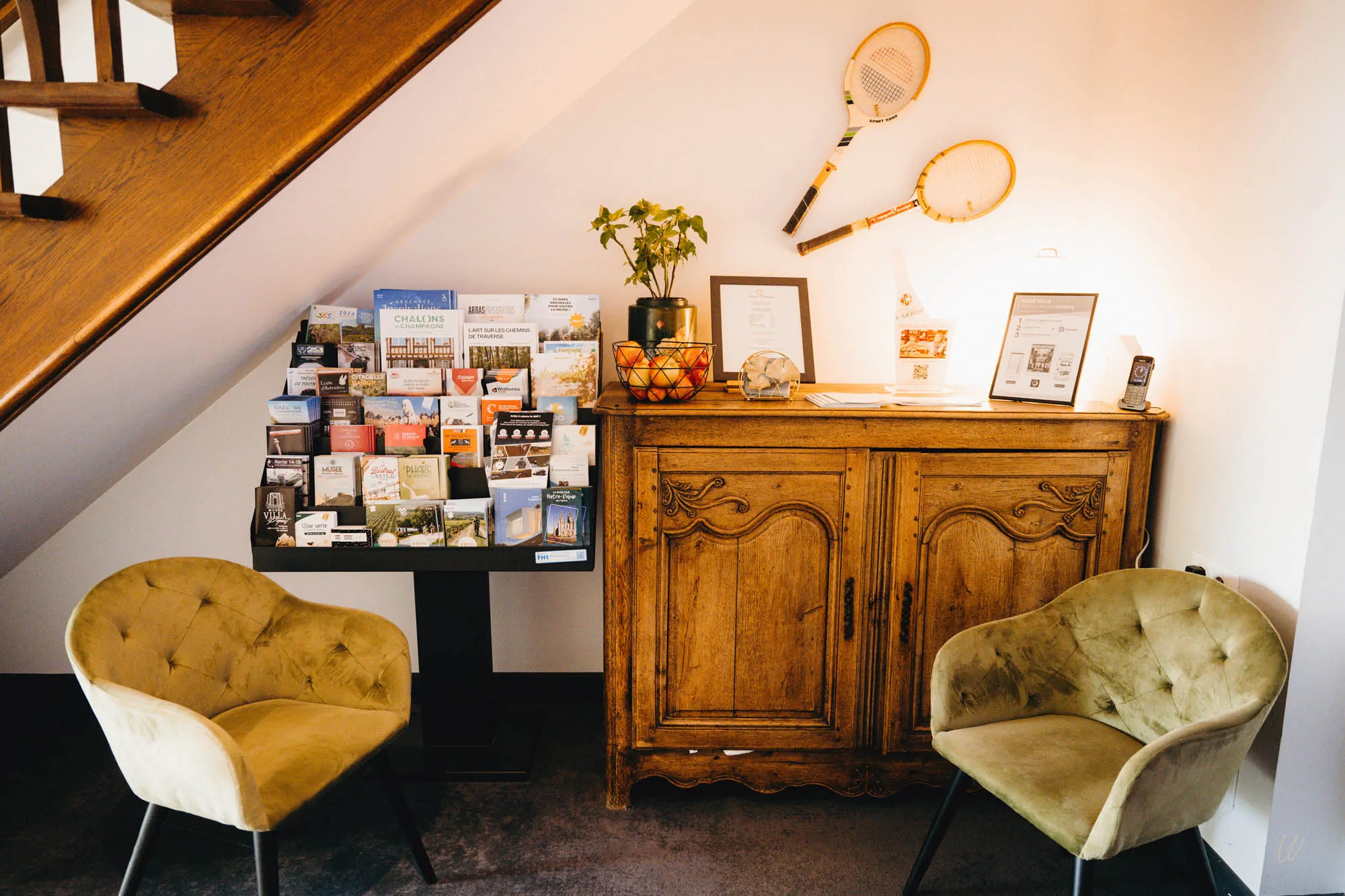 Coin accueil de l’hôtel Armes de Champagne avec brochures touristiques, fauteuils confortables et mobilier en bois sous l’escalier.