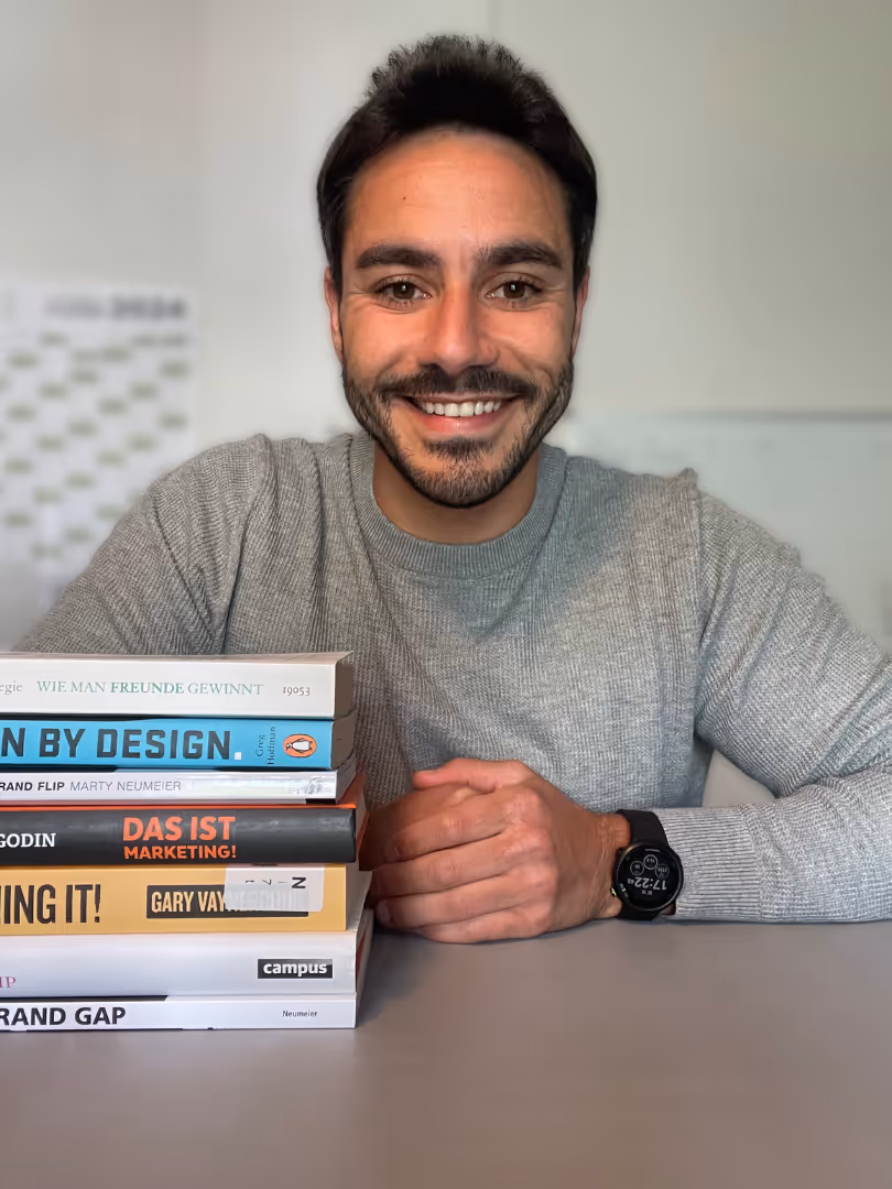 Ein Portrait von Mesut, stehen am Schreibtisch. Neben ihm liegen aufgestapelte Bücher.