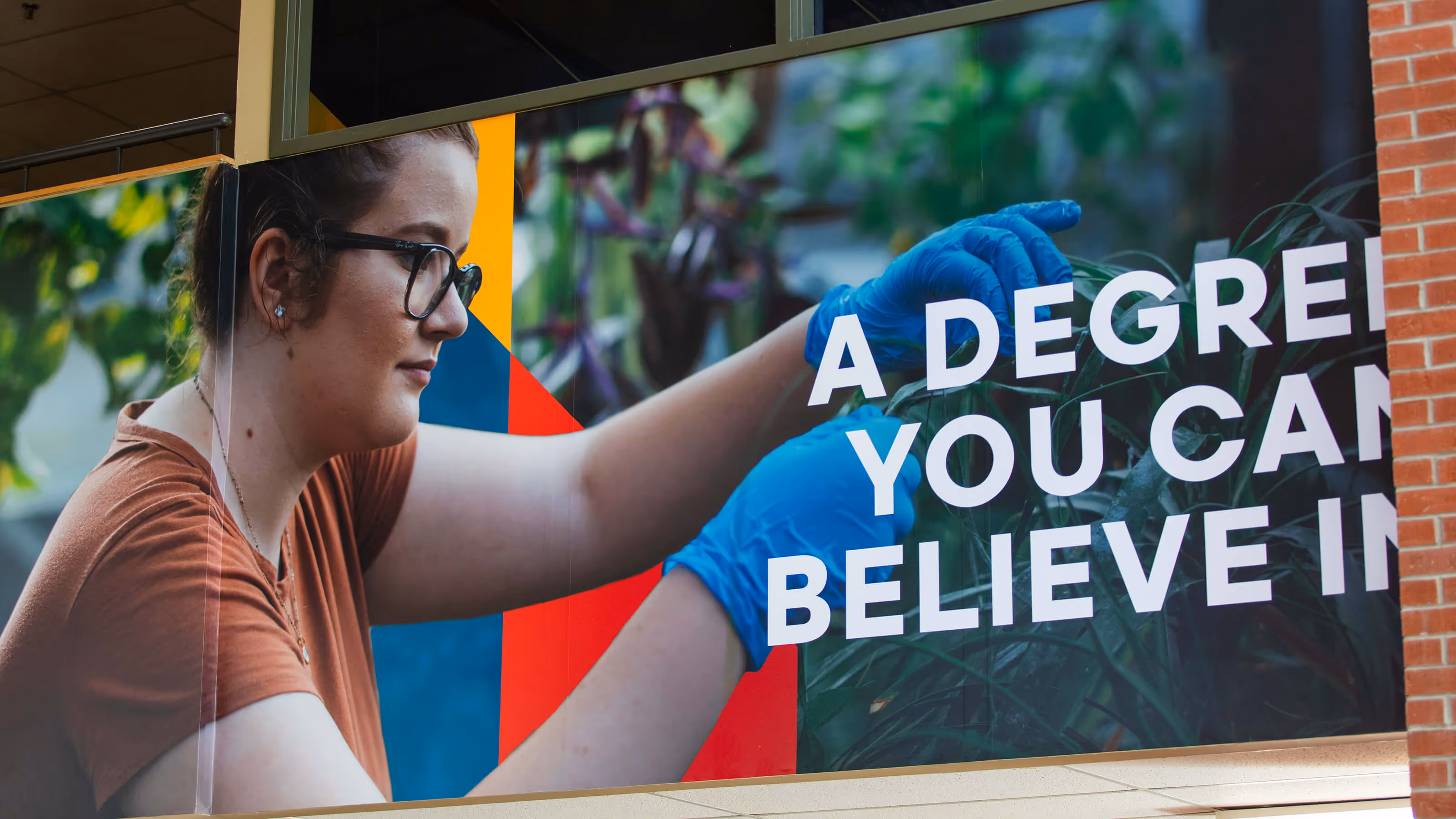 Woman wearing glasses and blue gloves tending to plants with text partially visible: 'A DEGREE YOU CAN BELIEVE IN.'