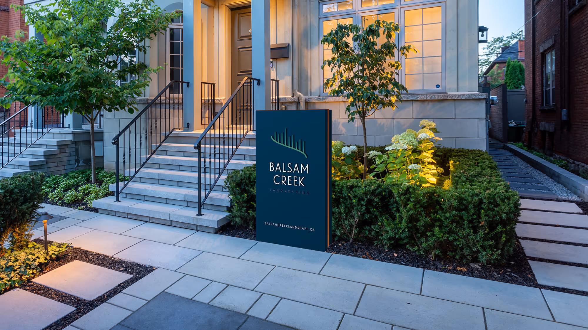 Front yard with stone steps, landscaped garden, and a Balsam Creek Landscaping sign near a tree.