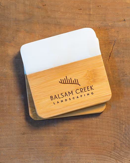 Rectangular wooden scraper with Balsam Creek Landscaping logo on a wooden surface.