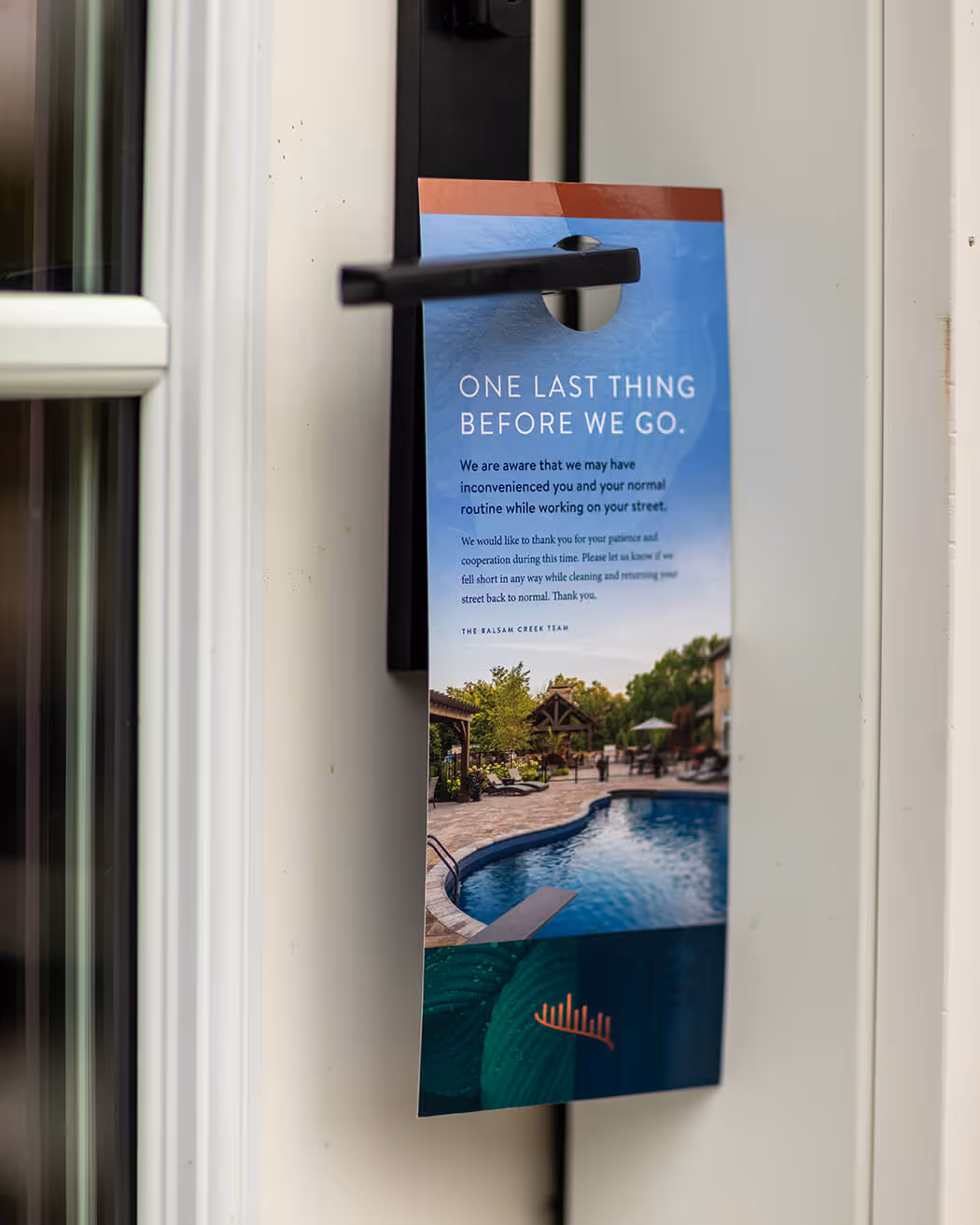 Door hanger on black door handle with message apologizing for inconvenience during street work, featuring poolside image.