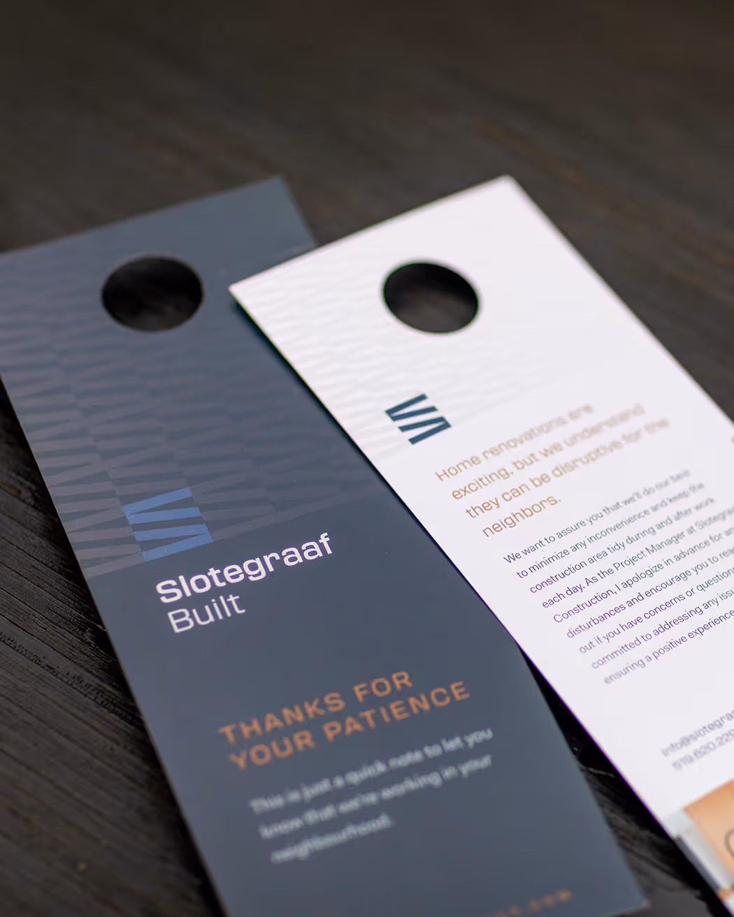 Two door hangers on a dark wooden surface, one black with 'Slotegraaf Built' and 'Thanks for your patience' text, and one white with information about home renovations.