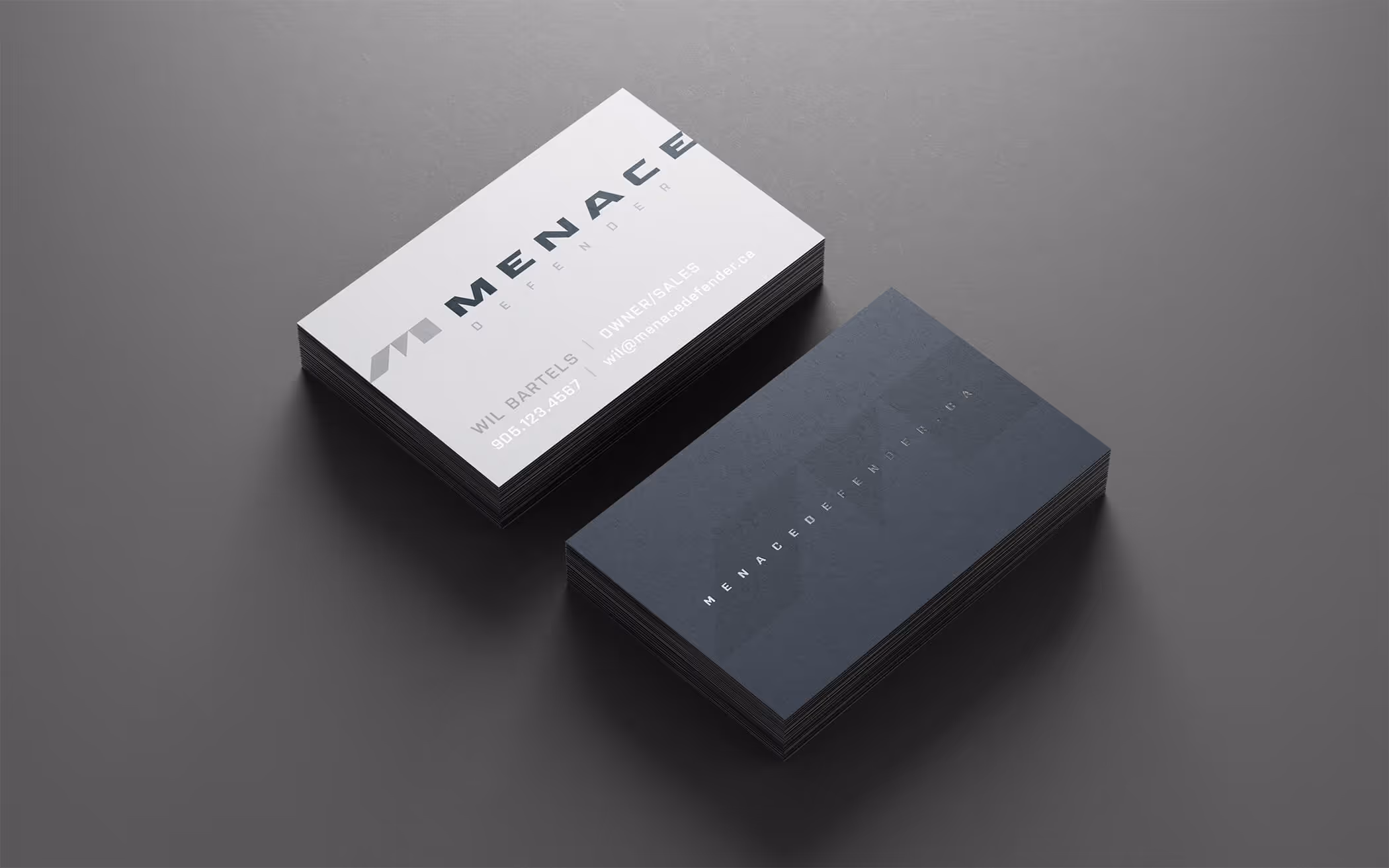 Two stacks of Menace Defender business cards on a gray surface, one showing contact details and logo, the other with website URL.