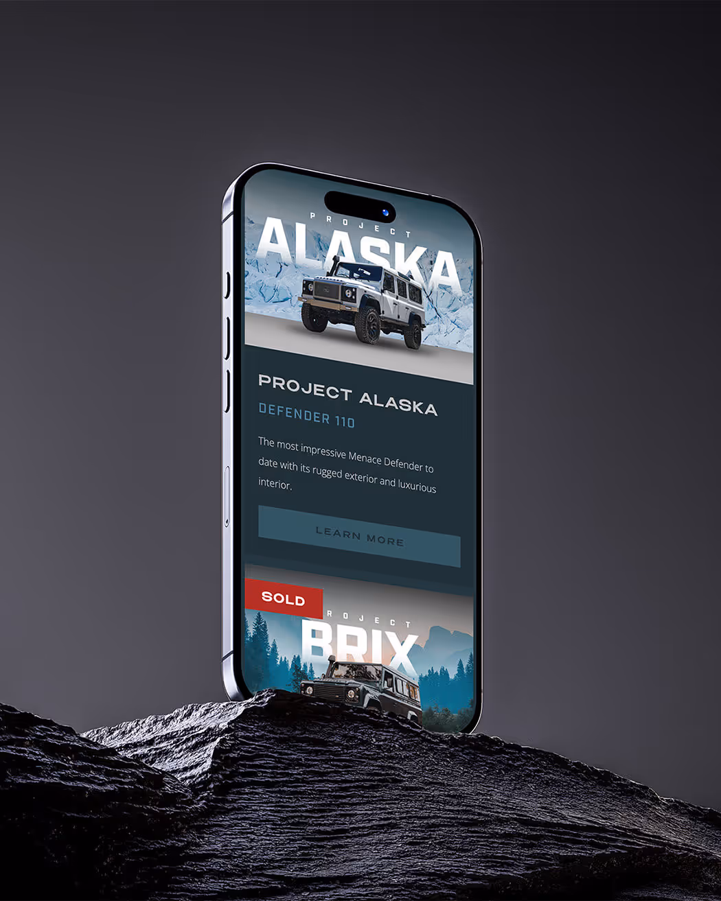 Smartphone displaying Project Alaska Defender 110 with a white rugged vehicle on icy background and a sold Project Brix vehicle on forest background.