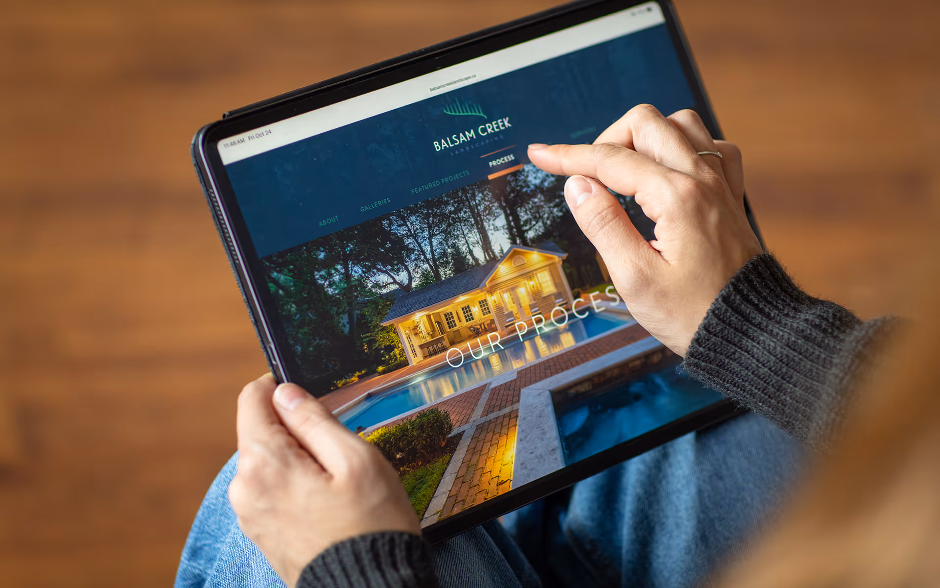 Person browsing Balsam Creek Landscaping website showing a lit backyard with pool on a tablet.