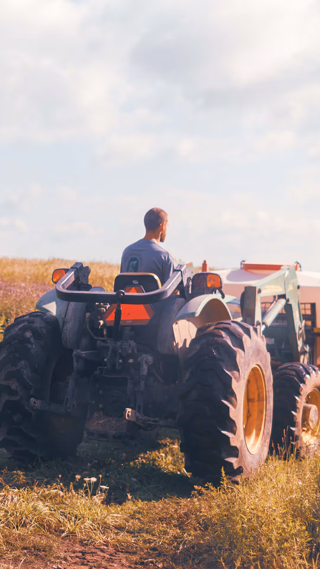 Man driving a tractor in a field under a partly cloudy sky.