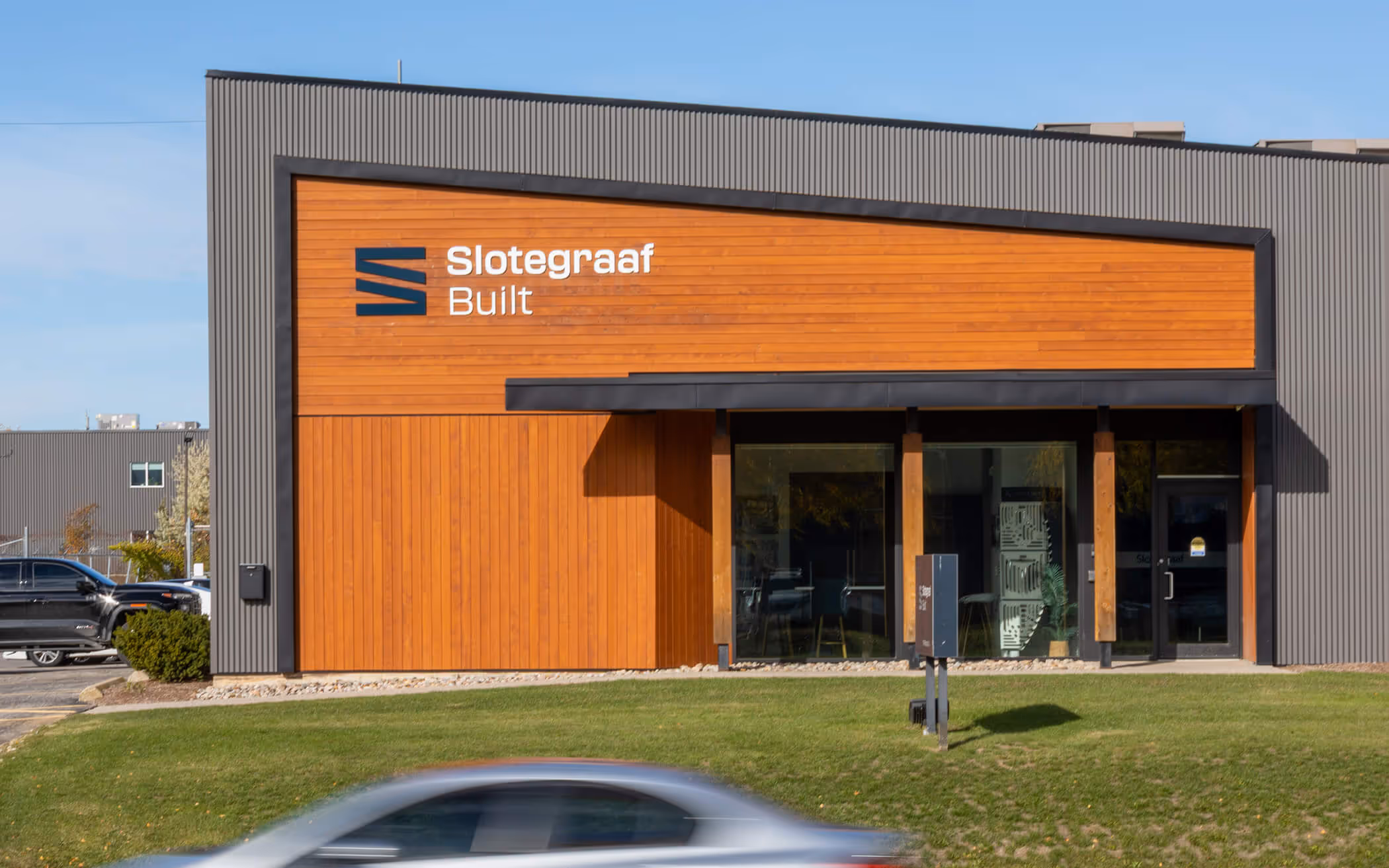 Modern commercial building with wood paneling and gray siding, featuring 'Slotegraaf Built' logo on the front.