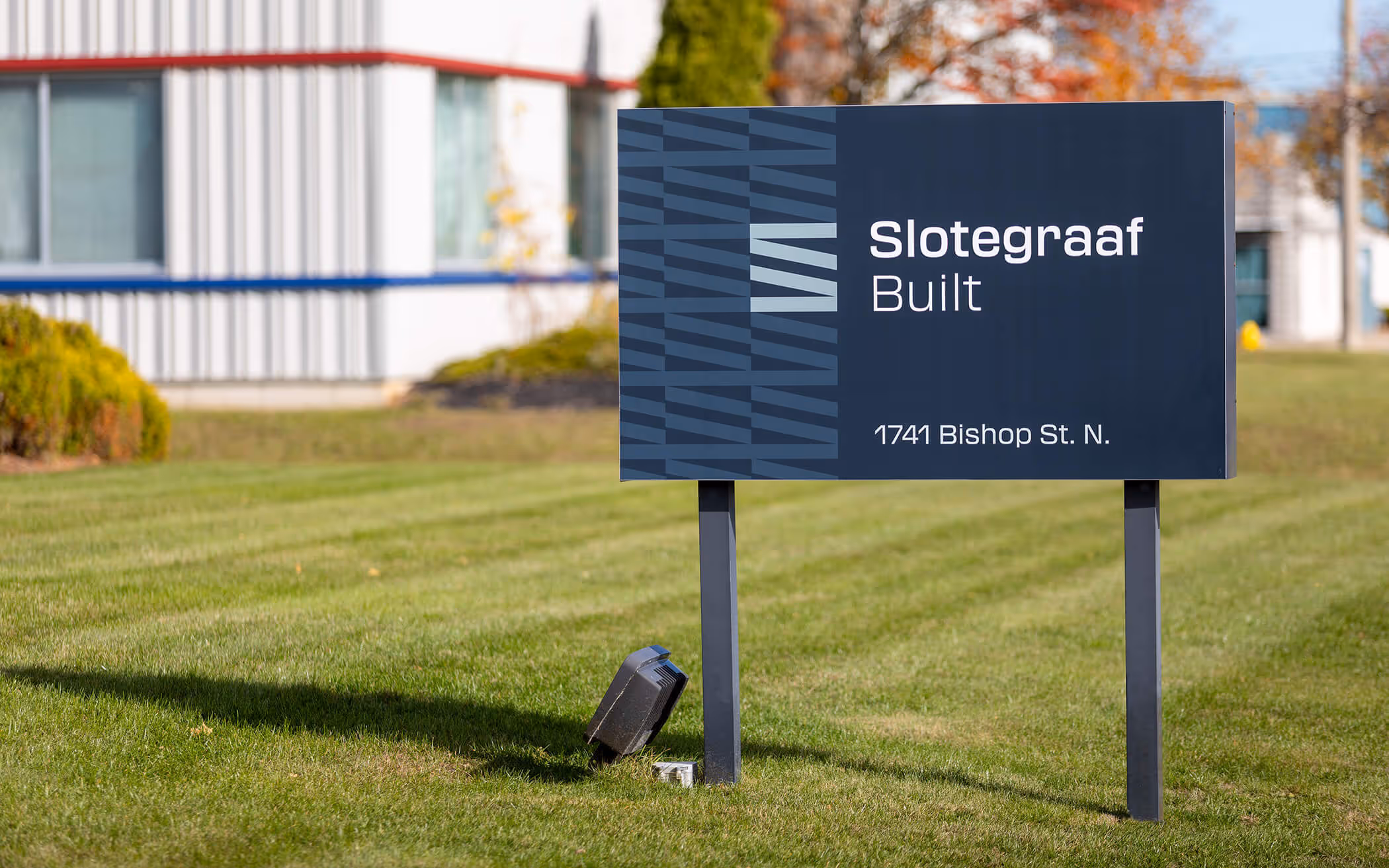 Outdoor sign on a grassy area reading 'Slotegraaf Built 1741 Bishop St. N.' with a patterned blue design on the left side.