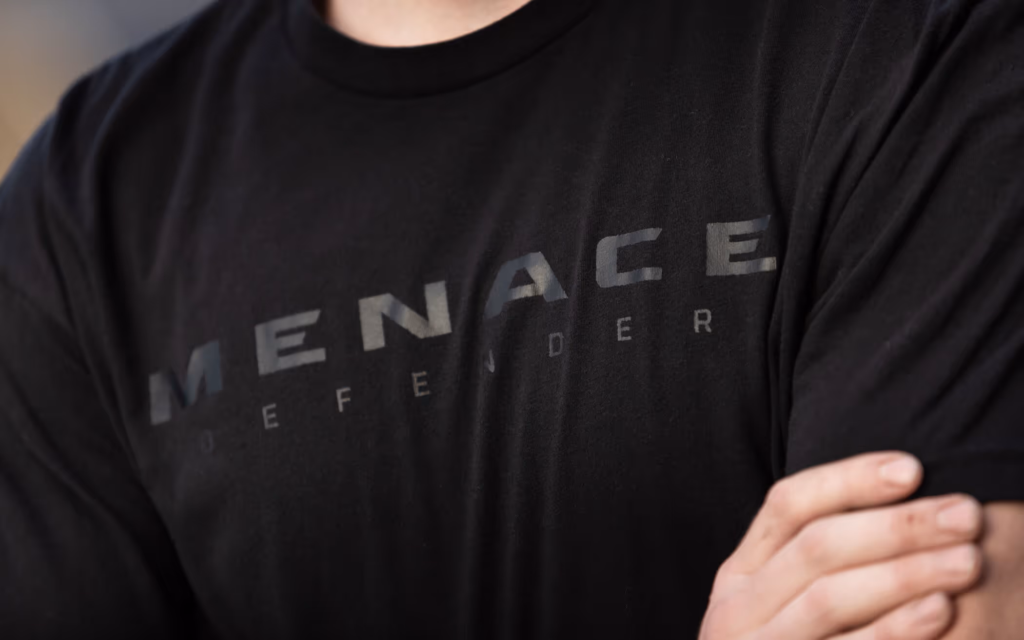 Close-up of a person wearing a black T-shirt with the word 'MENACE' printed across the chest.