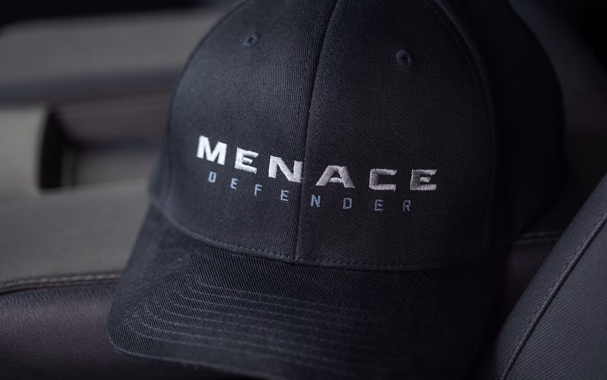 Black baseball cap with the words 'MENACE DEFENDER' embroidered in white and gray on the front.