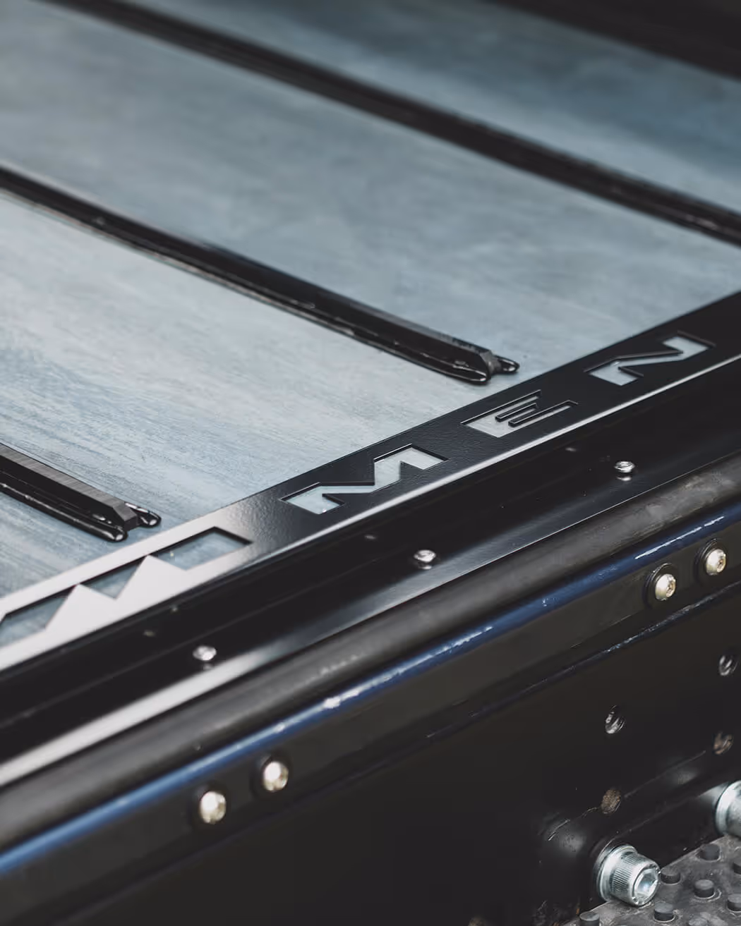 Close-up of a metallic surface with a black frame featuring cut-out letters and secured bolts.