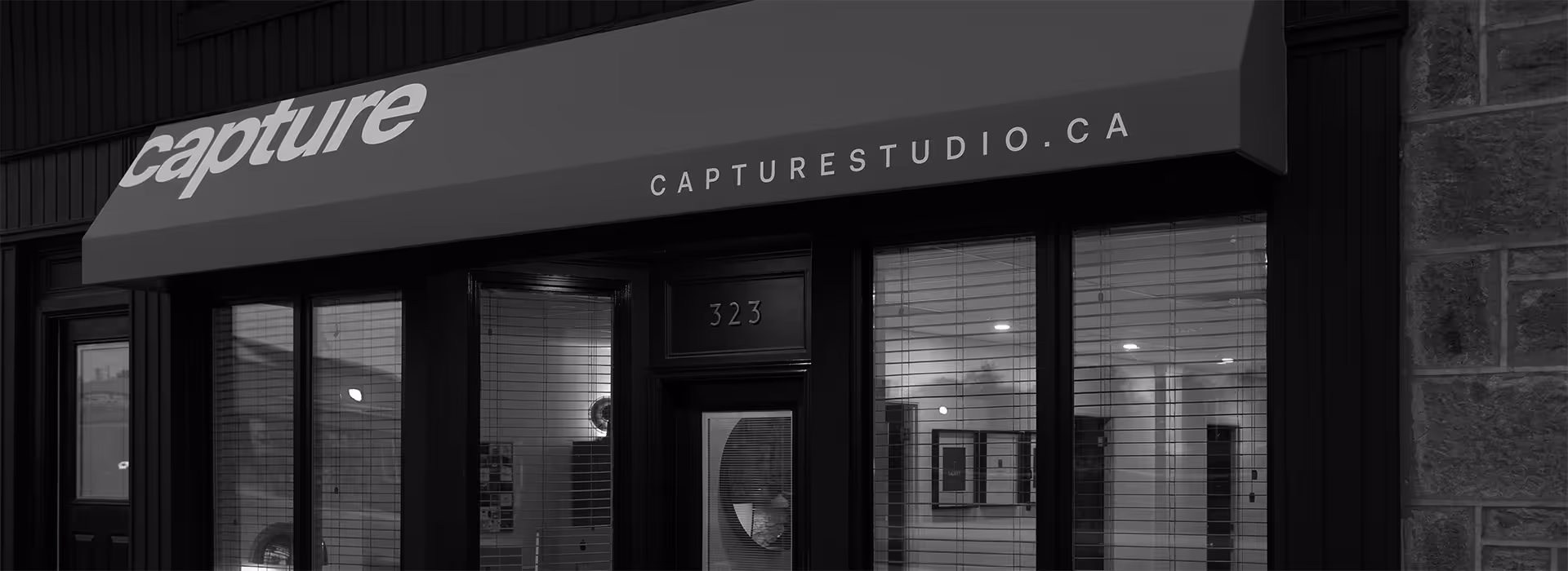 Entrance to a building with black framed glass windows and door under an orange awning reading 'capture' and 'capturestudio.ca', with the number 323 above the door.