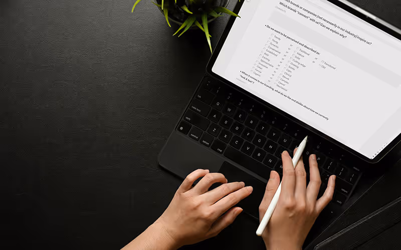 Person using a white stylus to interact with a tablet displaying a survey on a black textured desk with a green plant beside it.
