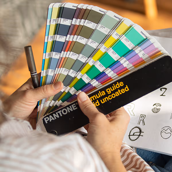 Person holding Pantone color swatches and a brown marker pen.