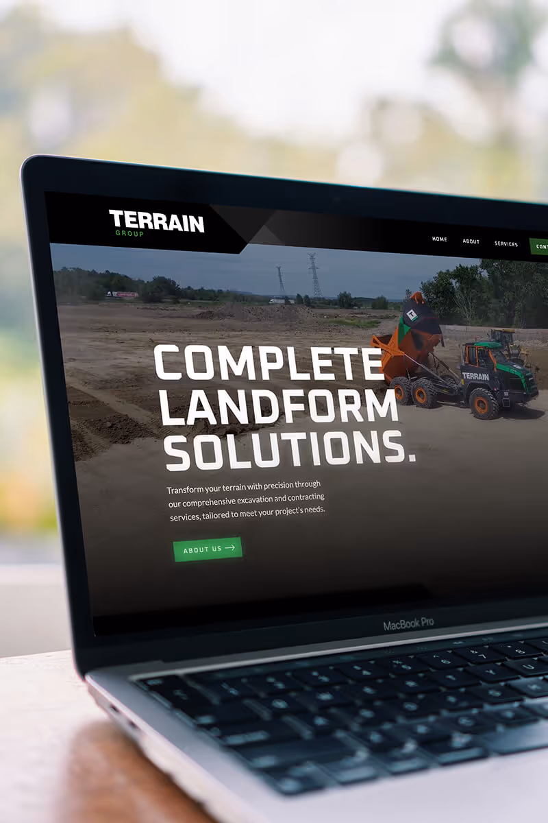 Laptop screen showing Terrain Group website with text 'Complete Landform Solutions' and an image of construction machinery on a dirt site.