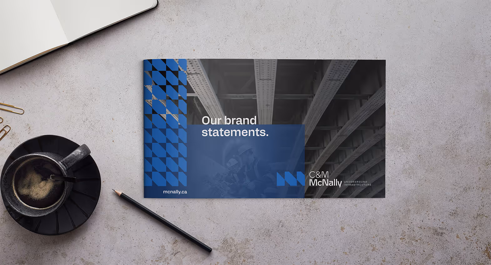Brochure on a gray surface with coffee cup, pencil, and paper clips; brochure features industrial beams with text 'Our brand statements.' and C&M McNally logo.