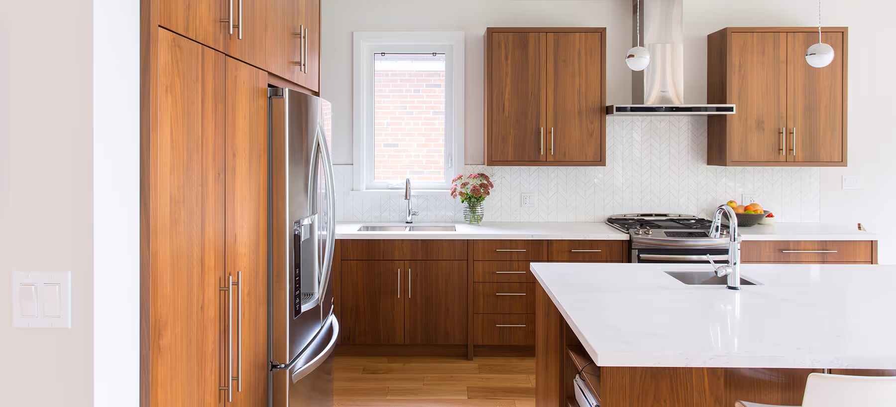 Modern kitchen with wood cabinets, stainless steel refrigerator, white countertops, small window, and two sinks.