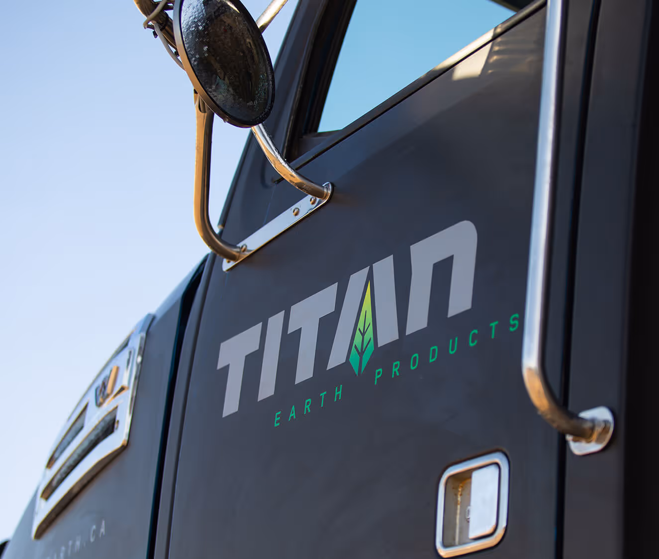 Close-up of a black vehicle door with the logo 'TITAN Earth Products' and a green leaf graphic, featuring a side mirror and door handle.