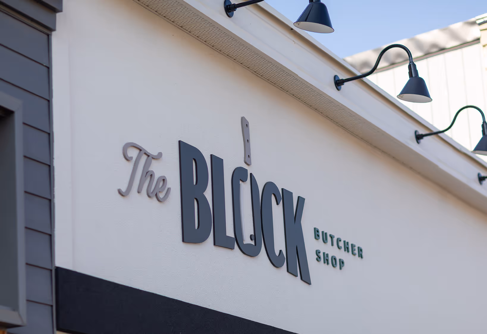 Exterior sign on a white building reading 'The BLUCK Butcher Shop' with the letter U stylized as a cleaver knife.