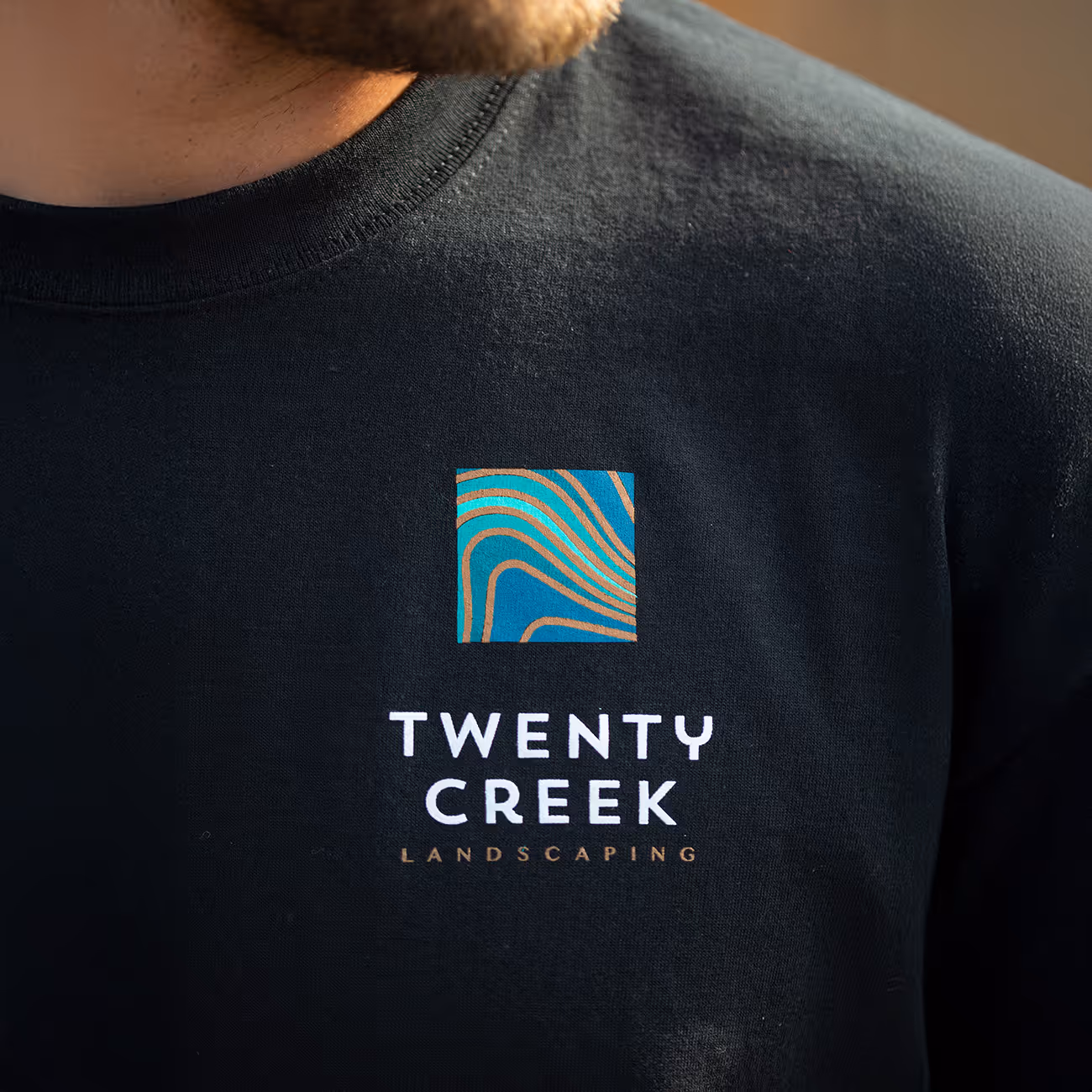 Close-up of a black shirt with a colorful square logo and the text 'TWENTY CREEK LANDSCAPING'.