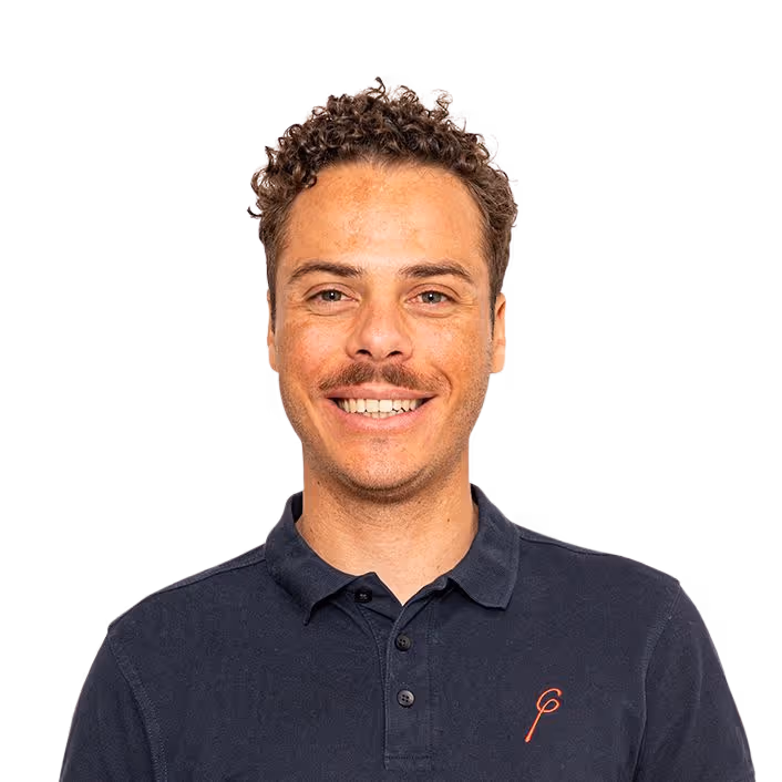 Smiling man with curly hair and a mustache wearing a dark polo shirt with a small red logo.