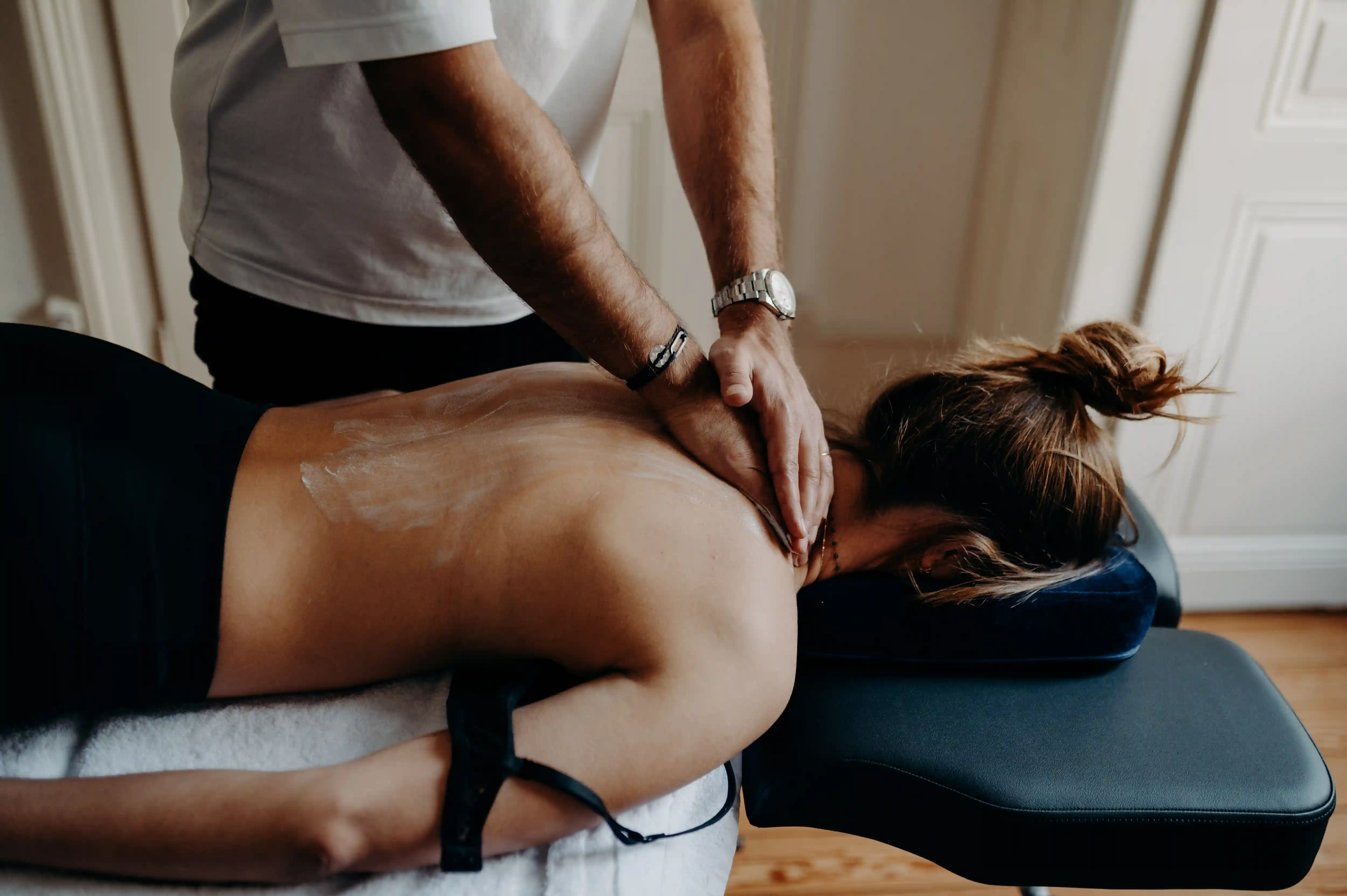 A person receiving a shoulder and upper back massage while lying face down on a massage table.