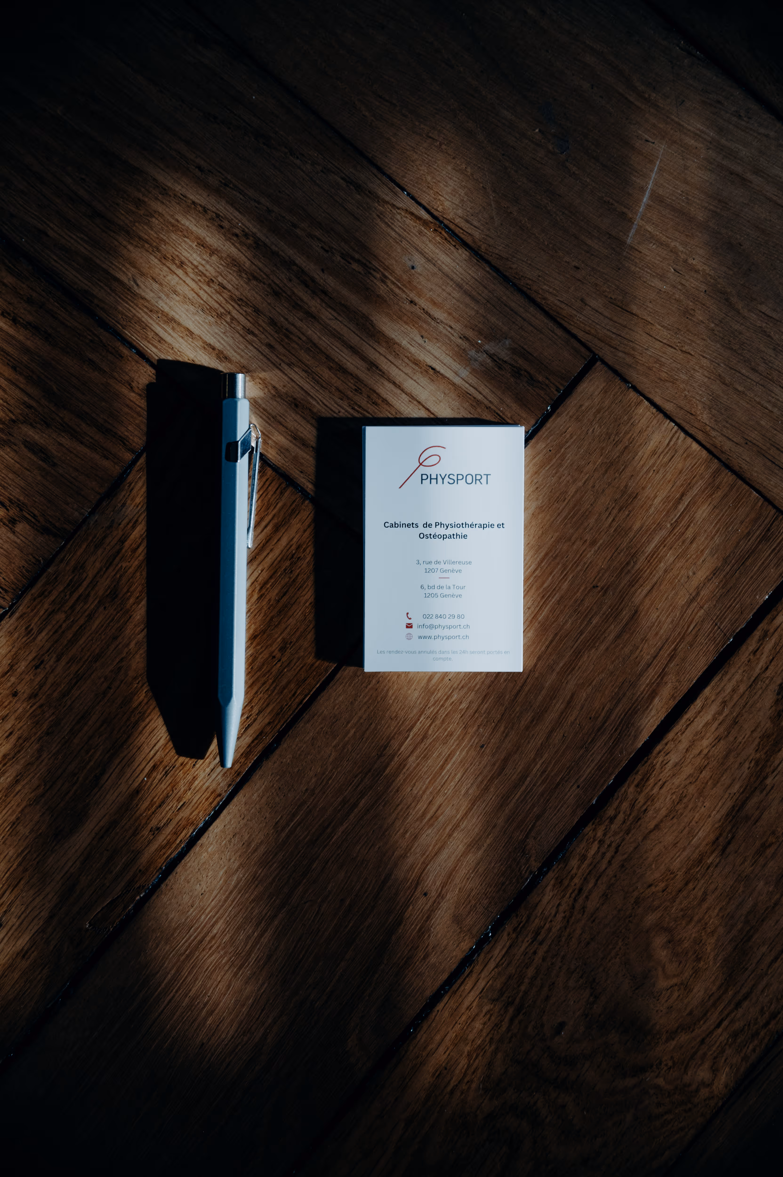 White pen and Physport business card on wooden floor with light and shadow.