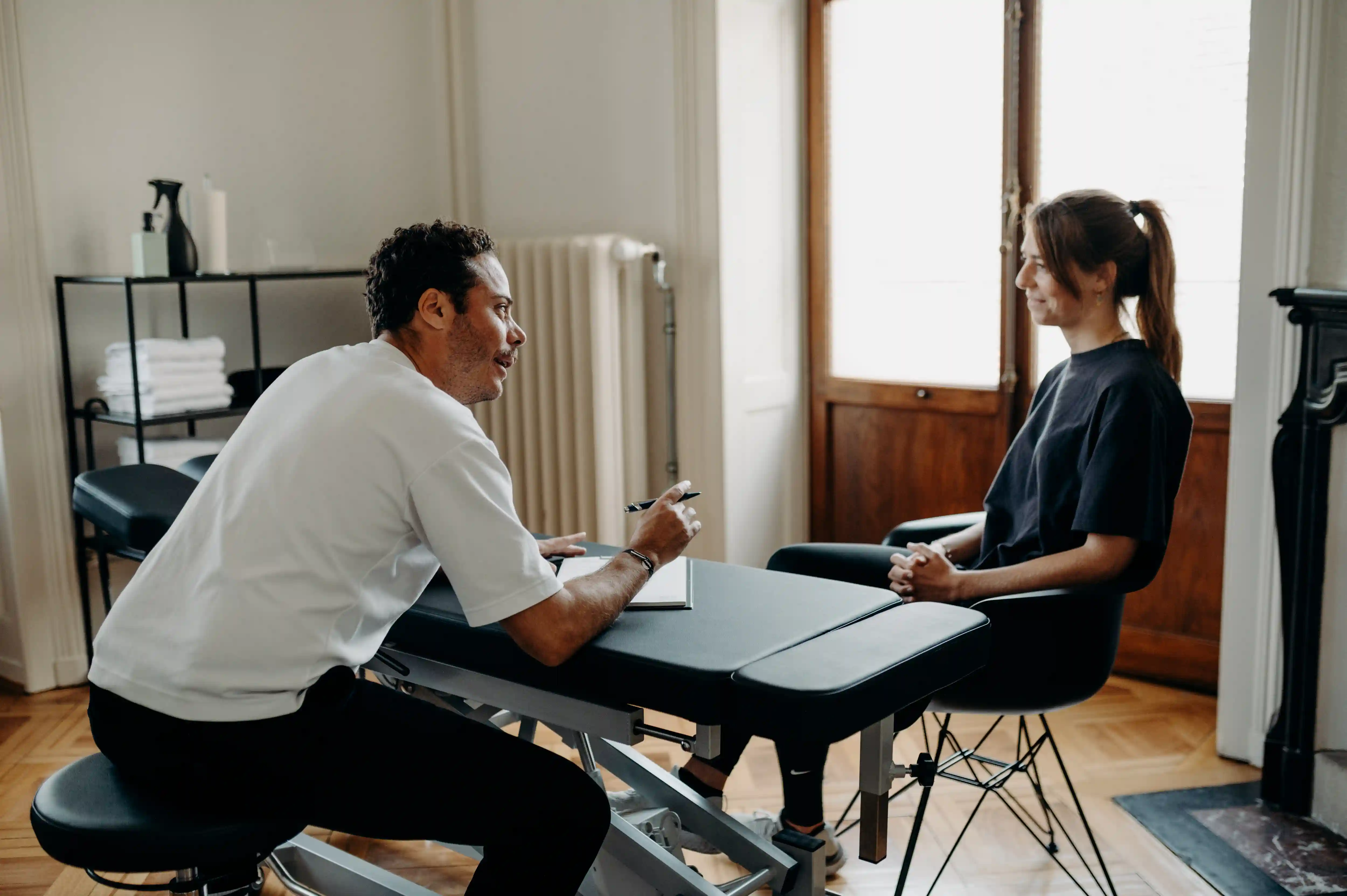 A therapist in a white shirt talking to and taking notes while a woman listens attentively in a seated consultation.