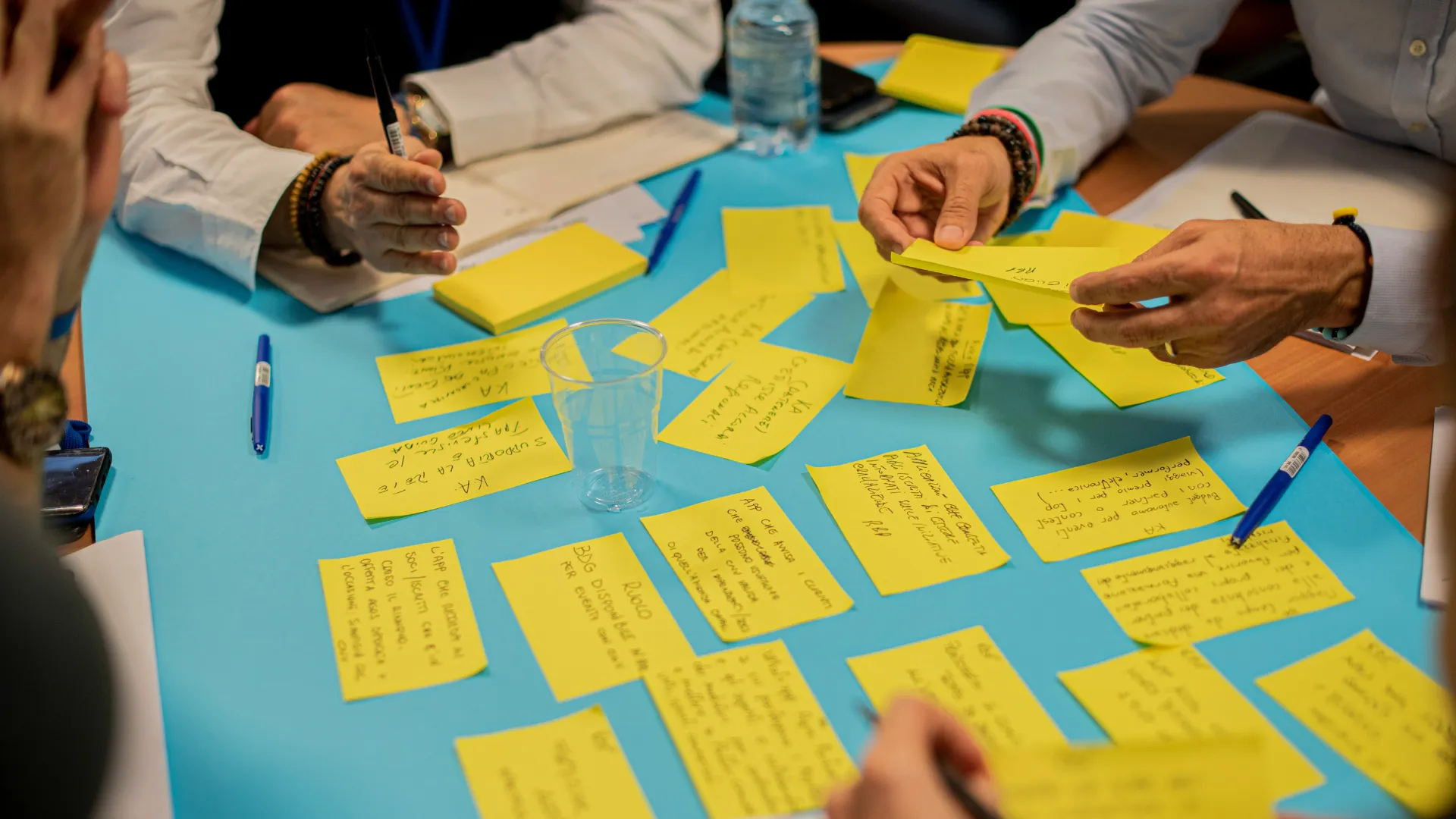 Menschen arbeiten zusammen an einem Tisch mit gelben Notizzetteln und blauen Stiften.