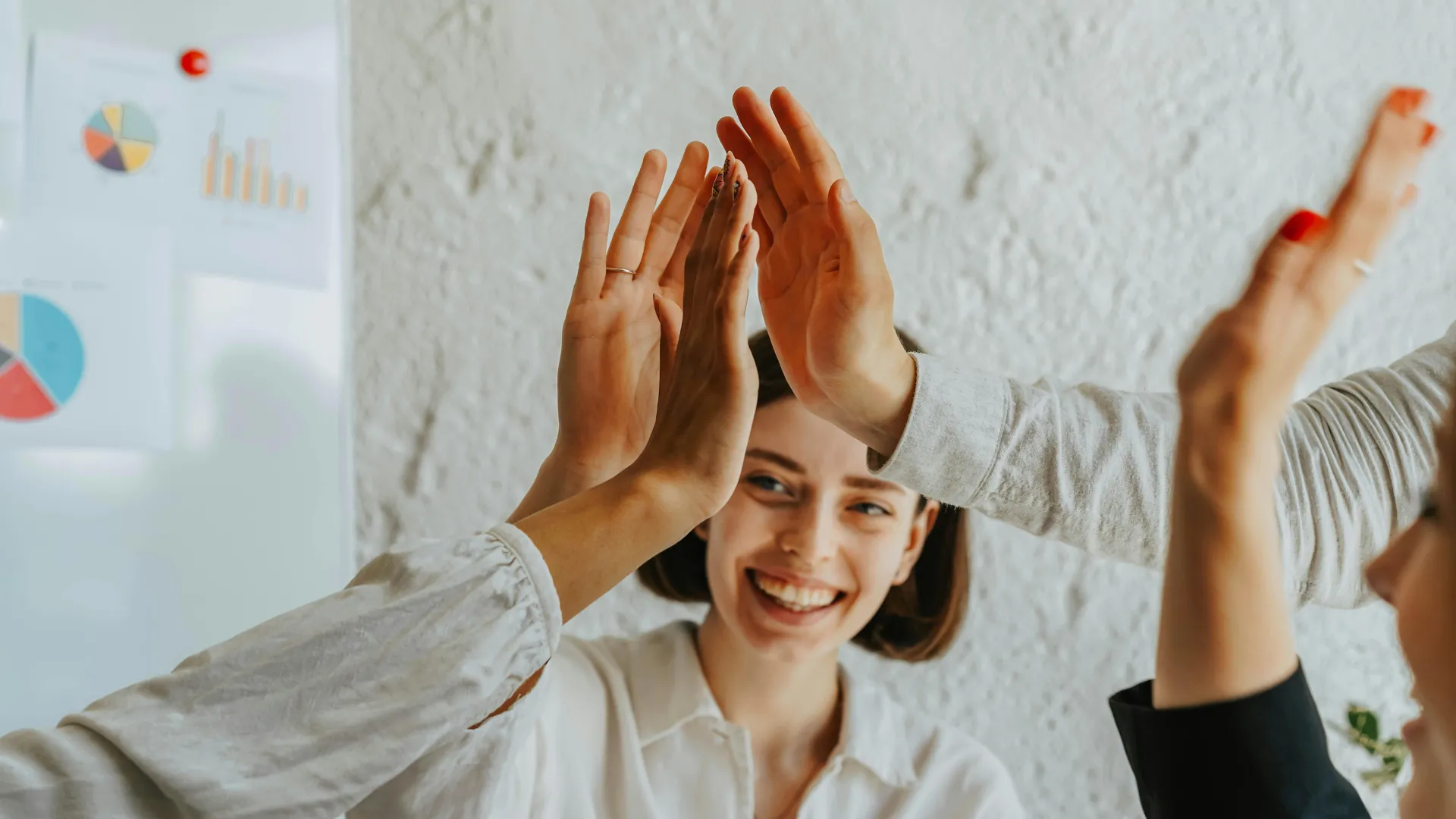 Drei Personen geben einander High Five, während eine lachende Frau im Hintergrund zu sehen ist.
