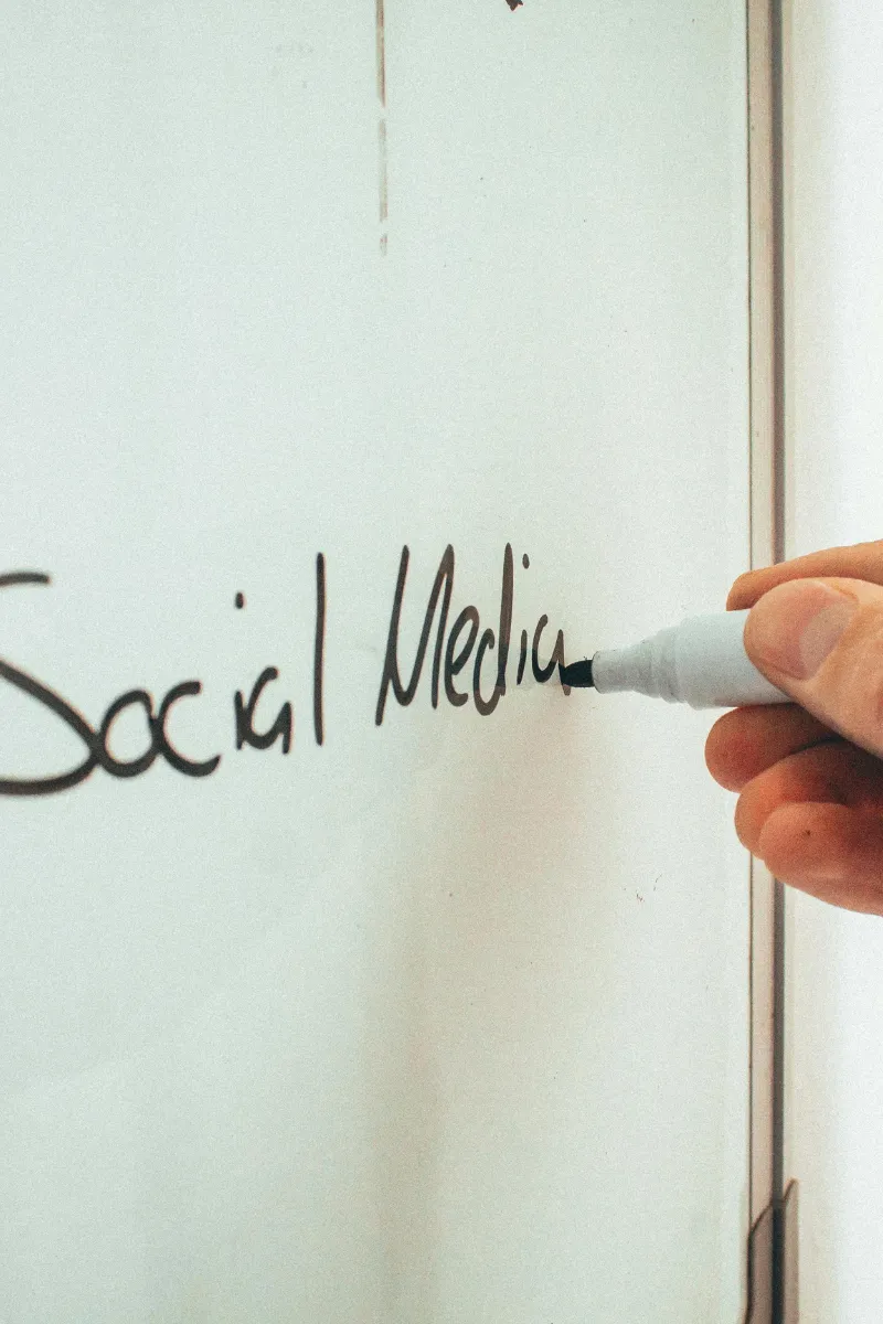 Hand writing the words Social Media with a black marker on a whiteboard.