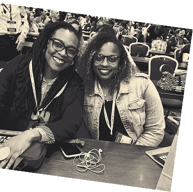 Two attendees at a How to Manage a Small Law Firm event, actively taking notes during a session. One man is wearing a dark sweater and glasses, while the other has light gray hair and a gray jacket. They are seated at a table with notebooks, pens, and water bottles, emphasizing the importance of learning and engagement in law firm management coaching.