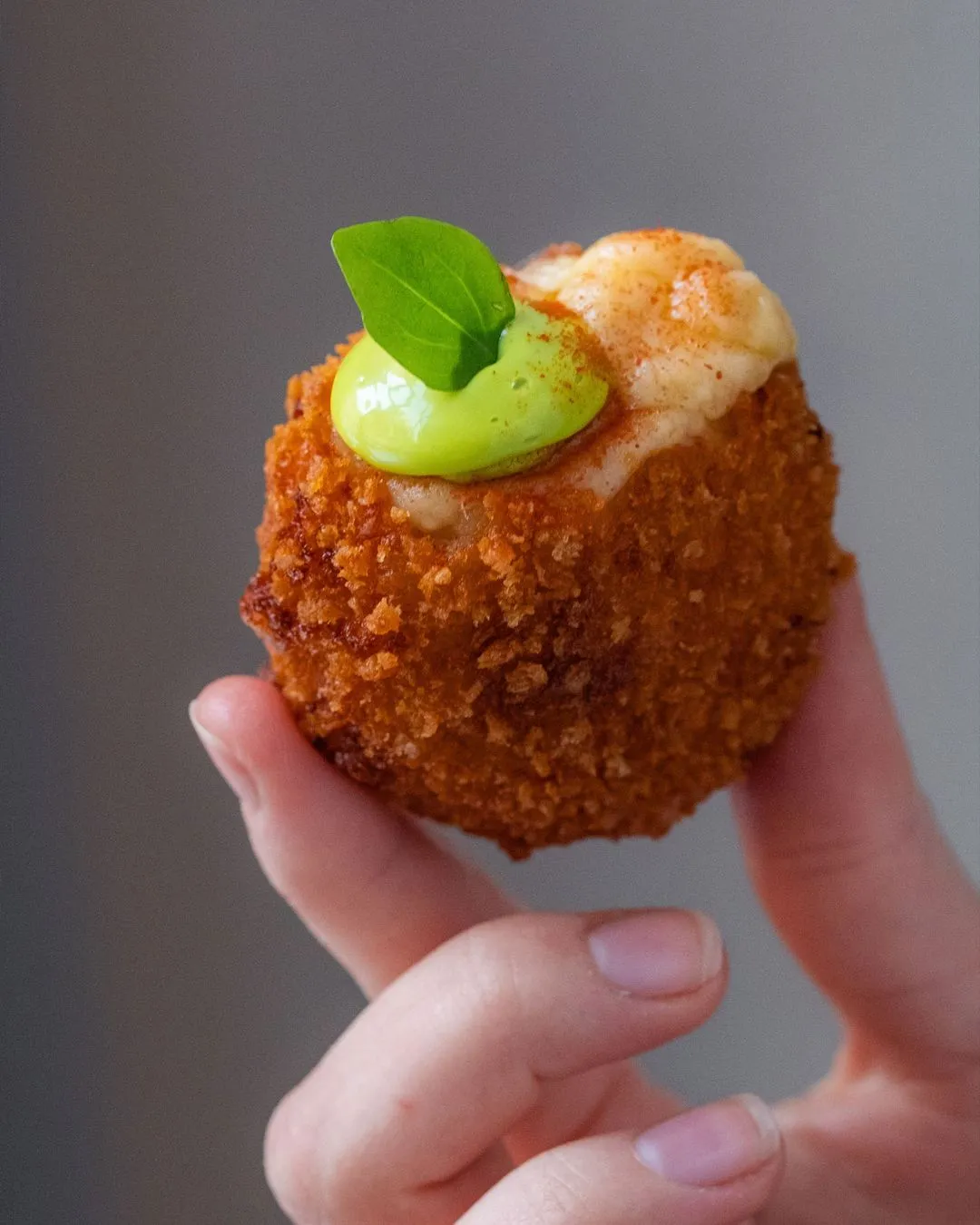 A hand holding a small piece of food with a green leaf on top.
