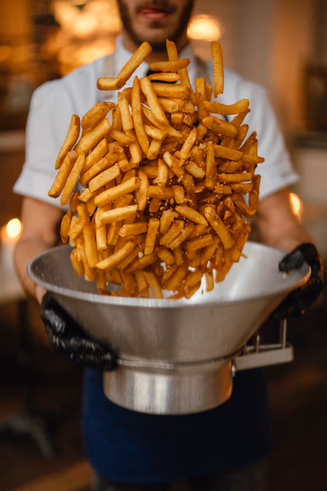 A man is pouring a large amount of french fries into a bowl.