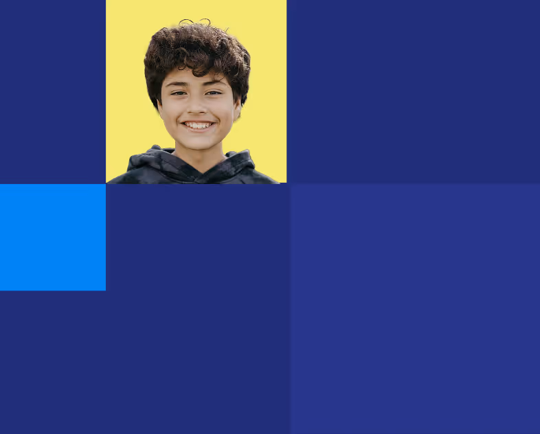 Smiling young boy with curly hair wearing a dark hoodie against a yellow background surrounded by blue blocks.