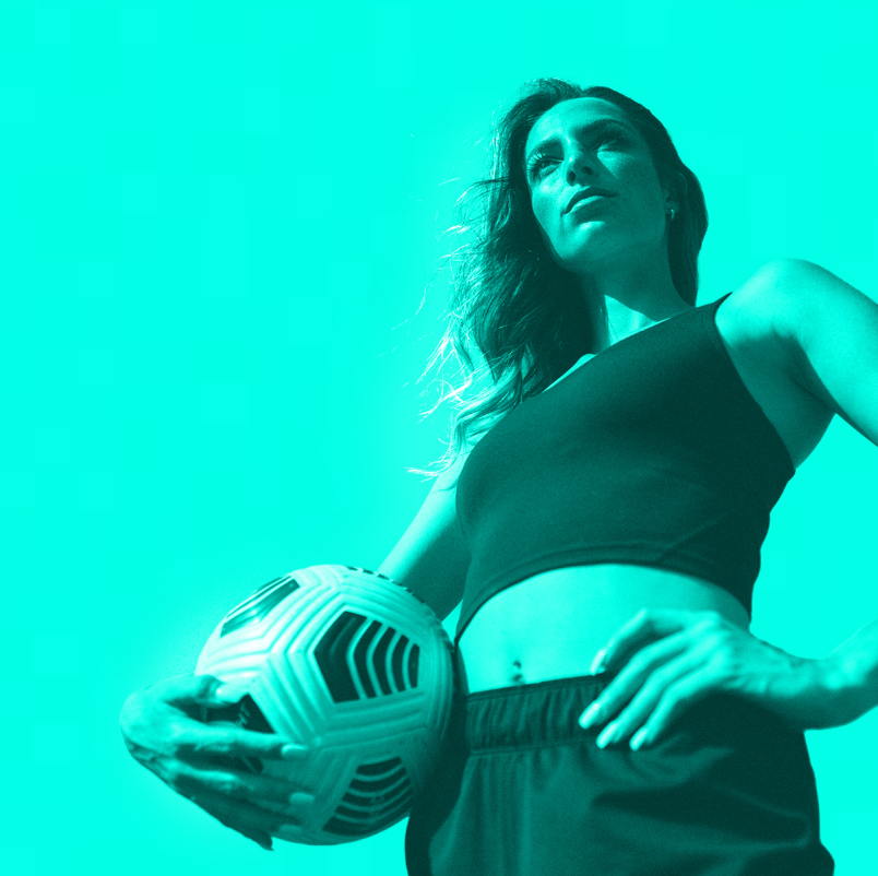 Image of a duotoned woman in green from the waist up, holding a soccer ball.