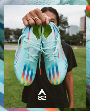 Shot of a woman holding up a pair of soccer shoes to the camera.