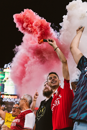 Fans at a soccer game holding smokeing cans.