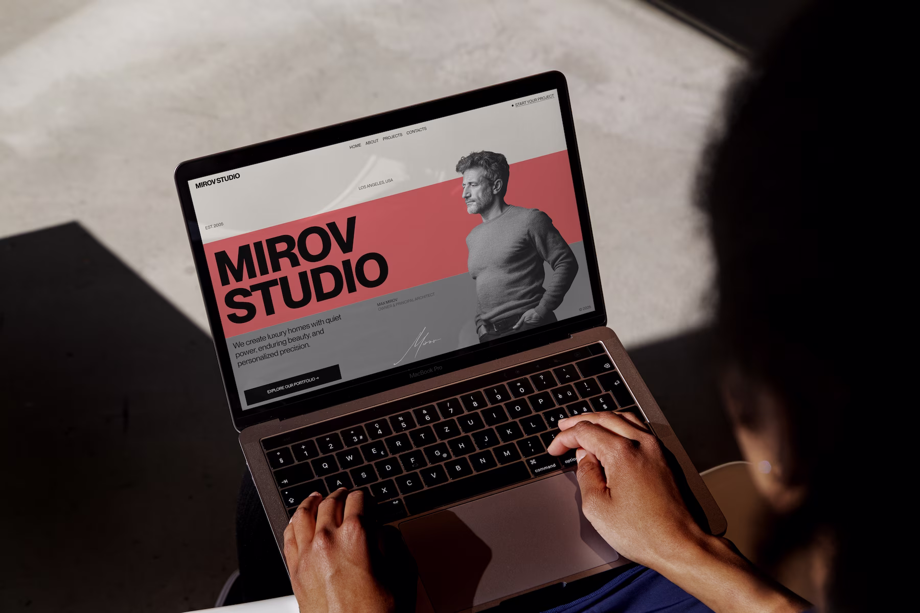 Close-up of a laptop screen displaying the MIROV STUDIO website, featuring bold text and a profile silhouette on a red and gray background, with a person interacting with the laptop.