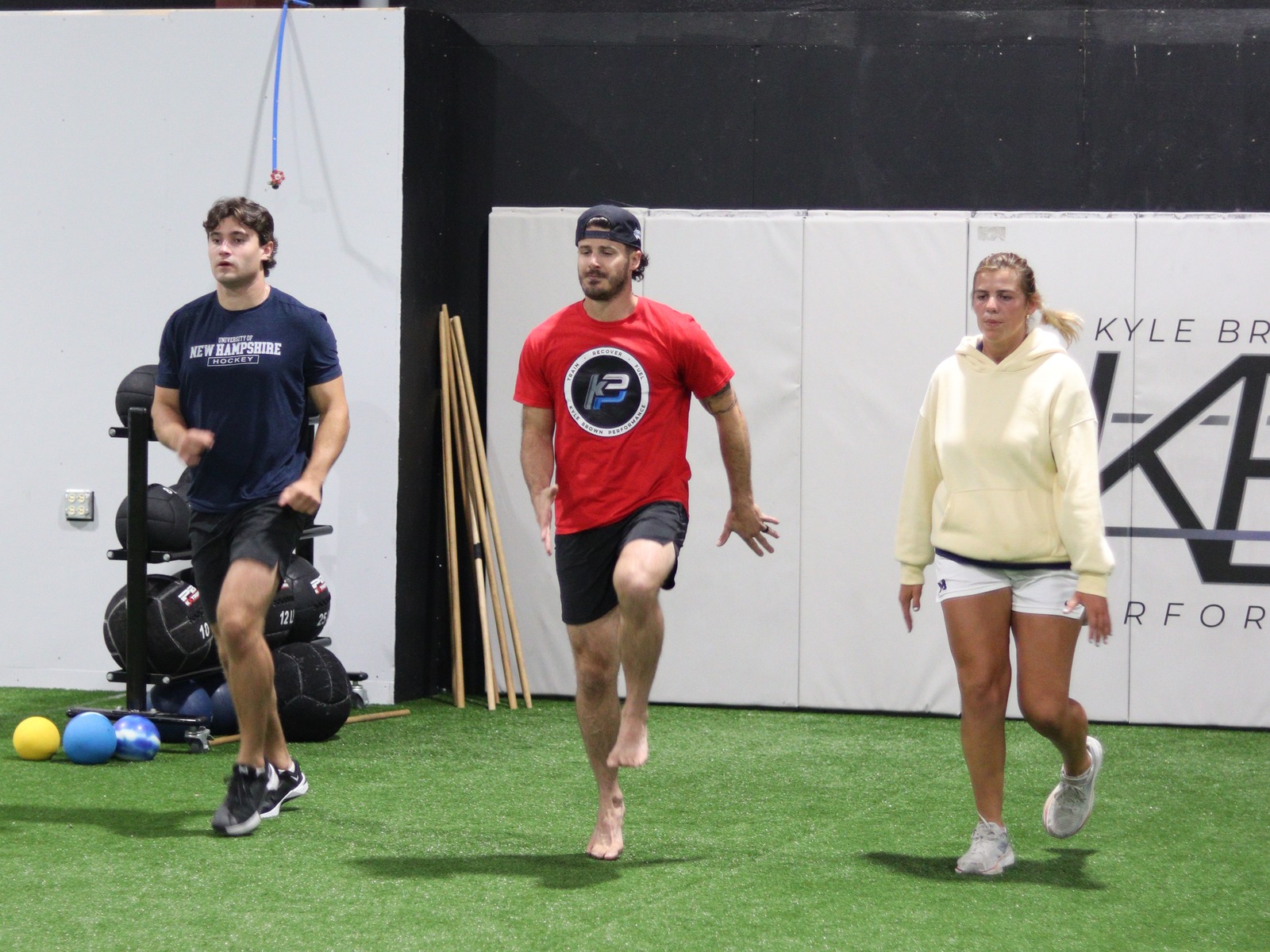 KBP athletes practicing knee-drive mechanics with a coach on the turf.