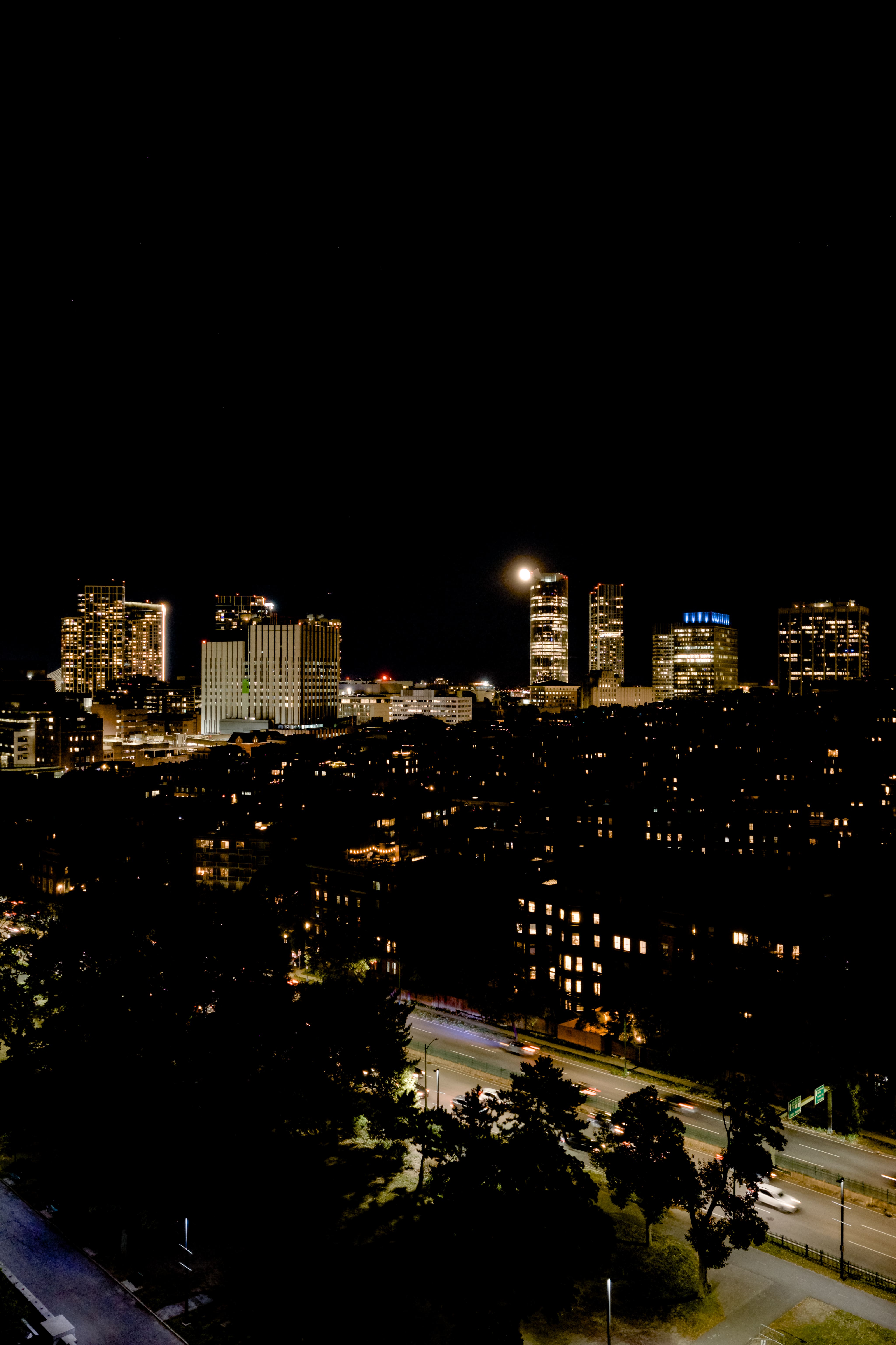 Professional nighttime drone image of the Boston skyline with the moon behind a building