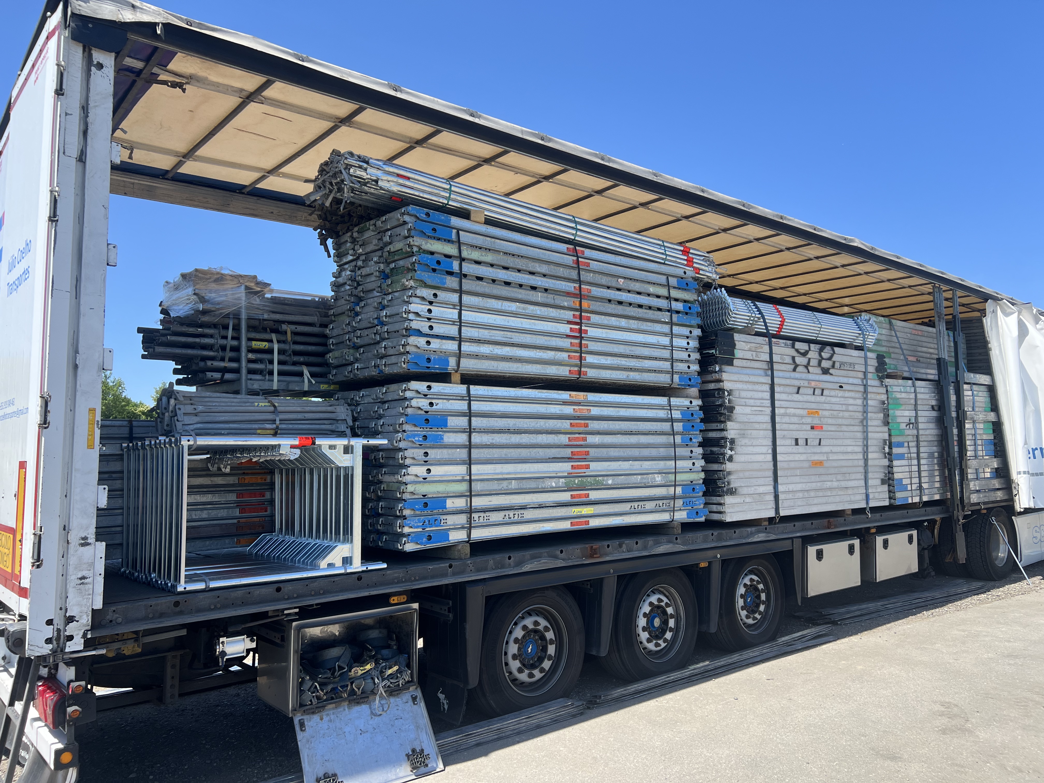 Flatbed truck loaded with stacks of metal scaffolding and equipment under a blue sky.