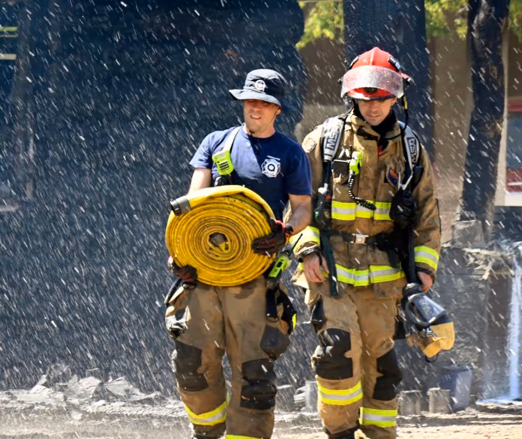 Two firefighters work together to carry a heavy hose towards a fire scene.